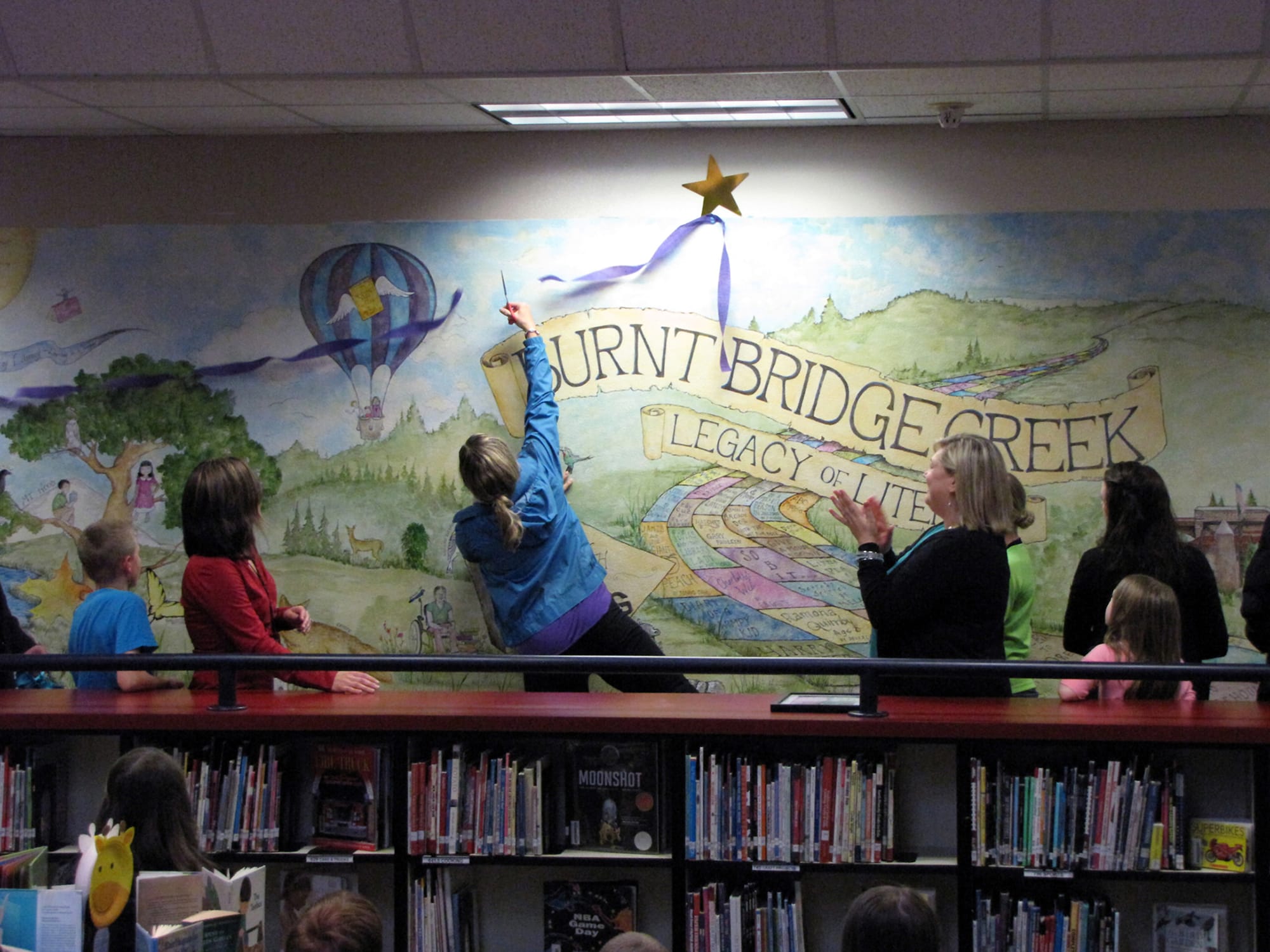 Students and staff at Burnt Bridge Creek Elementary School celebrate the unveiling of a new mural in their library painted by parent Eve Ellis-Carlson.