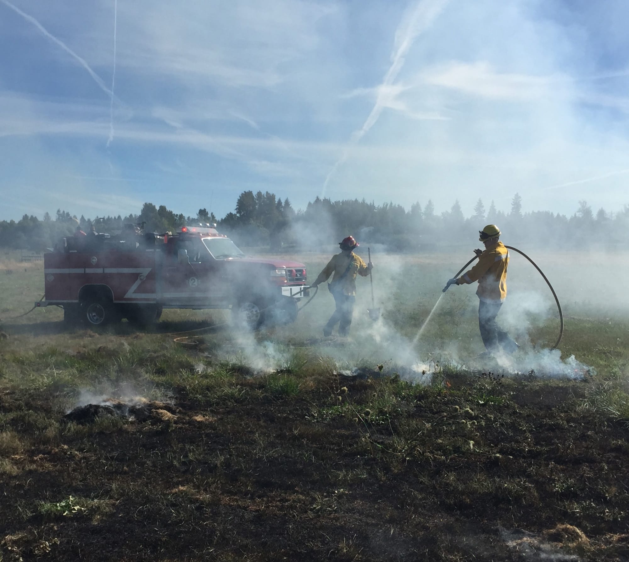 Clark County Fire & RescueFirefighters spray down a grass fire in a field west of Battle Ground on Tuesday afternoon.