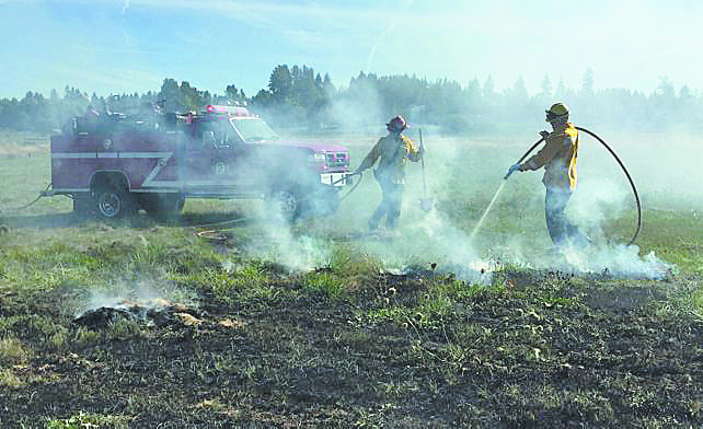 Firefighters spray down a grass fire in a field west of Battle Ground Tuesday afternoon.