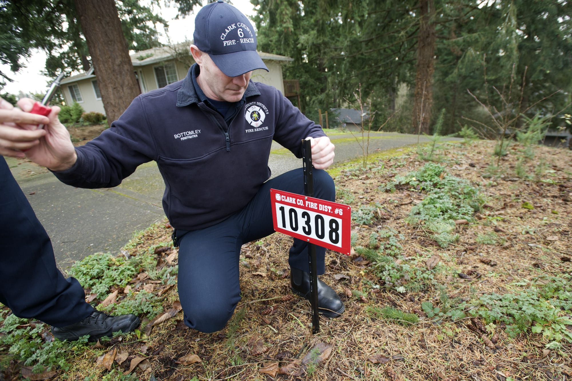 Fire District 6 Firefighter Chris Bottomley places a reflective address sign near a driveway in Hazel Dell.