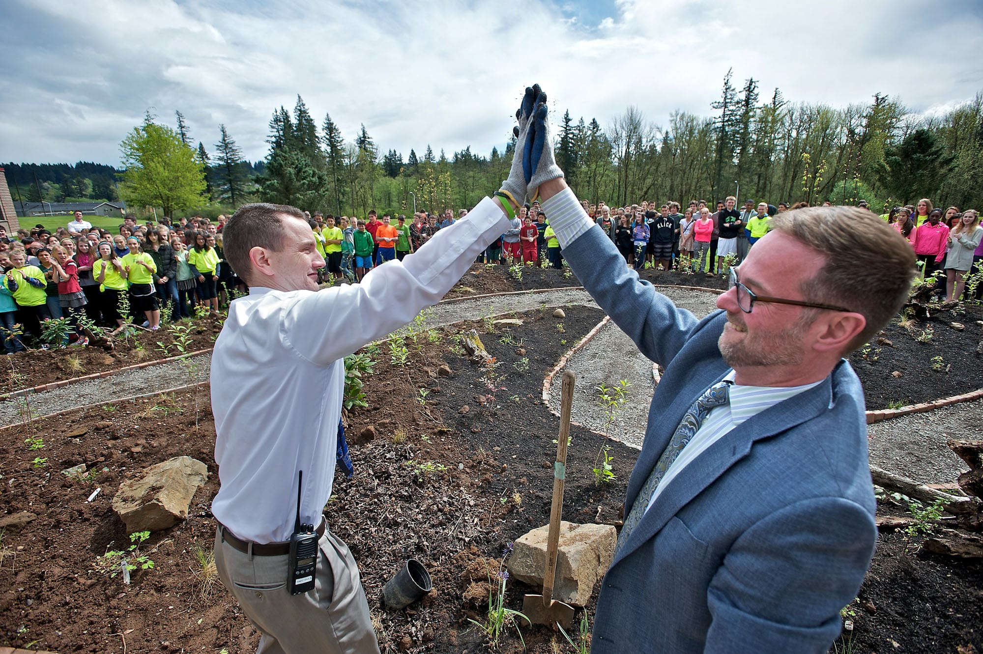 Skyridge Middle School Associate Principal Clint Williams, left, and Principal Aaron Smith give each other a high-five Tuesday after planting two camas lilies, signifying the completion of the Skyridge Lewis and Clark native plant garden, during a ceremony coinciding with Earth Day.