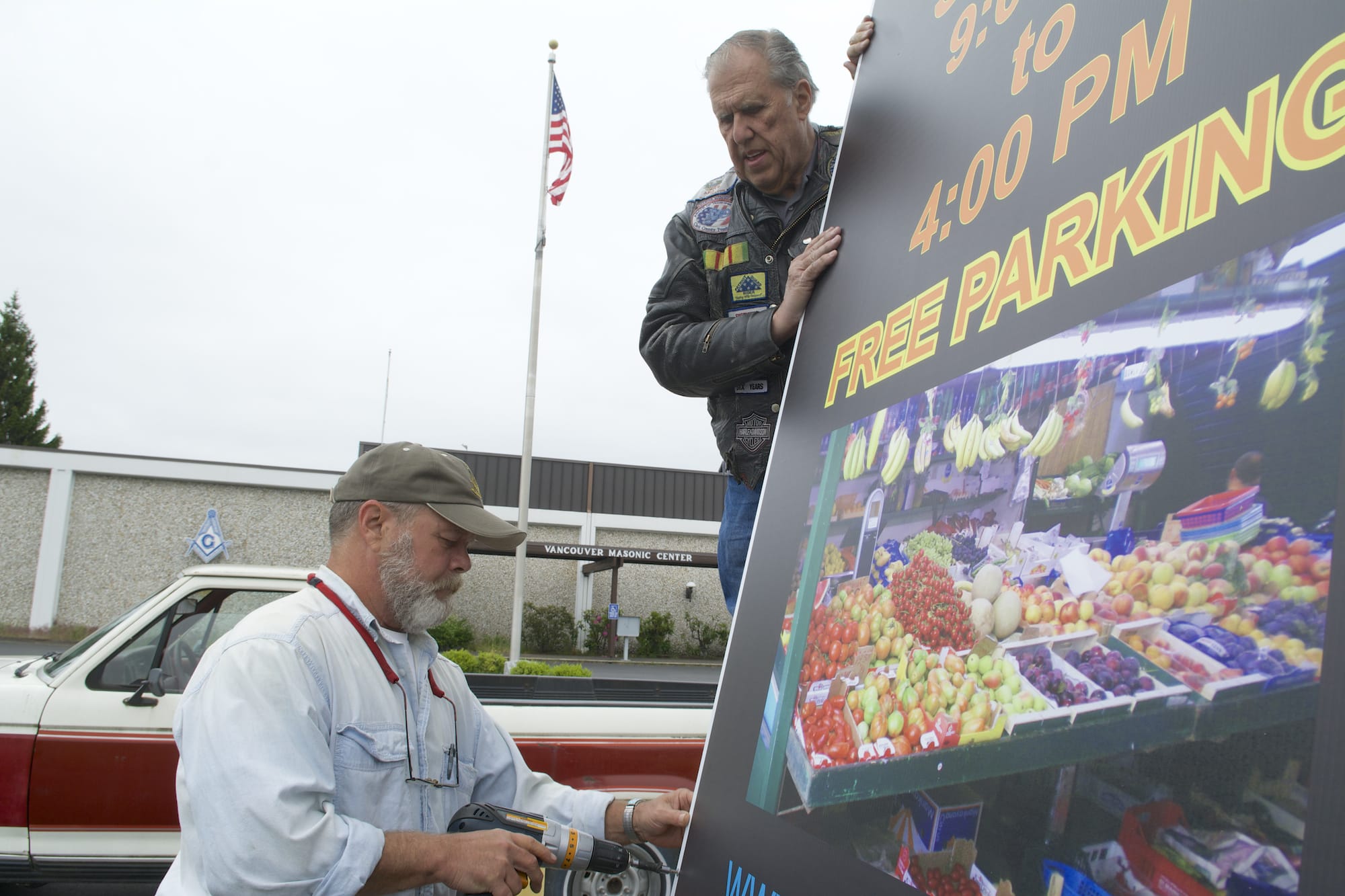 Ron Fryer, top, and Jimmy Johnson hang a farmers market sign outside the Vancouver Masonic Center in Hazel Dell in preparation of its kickoff Saturday.