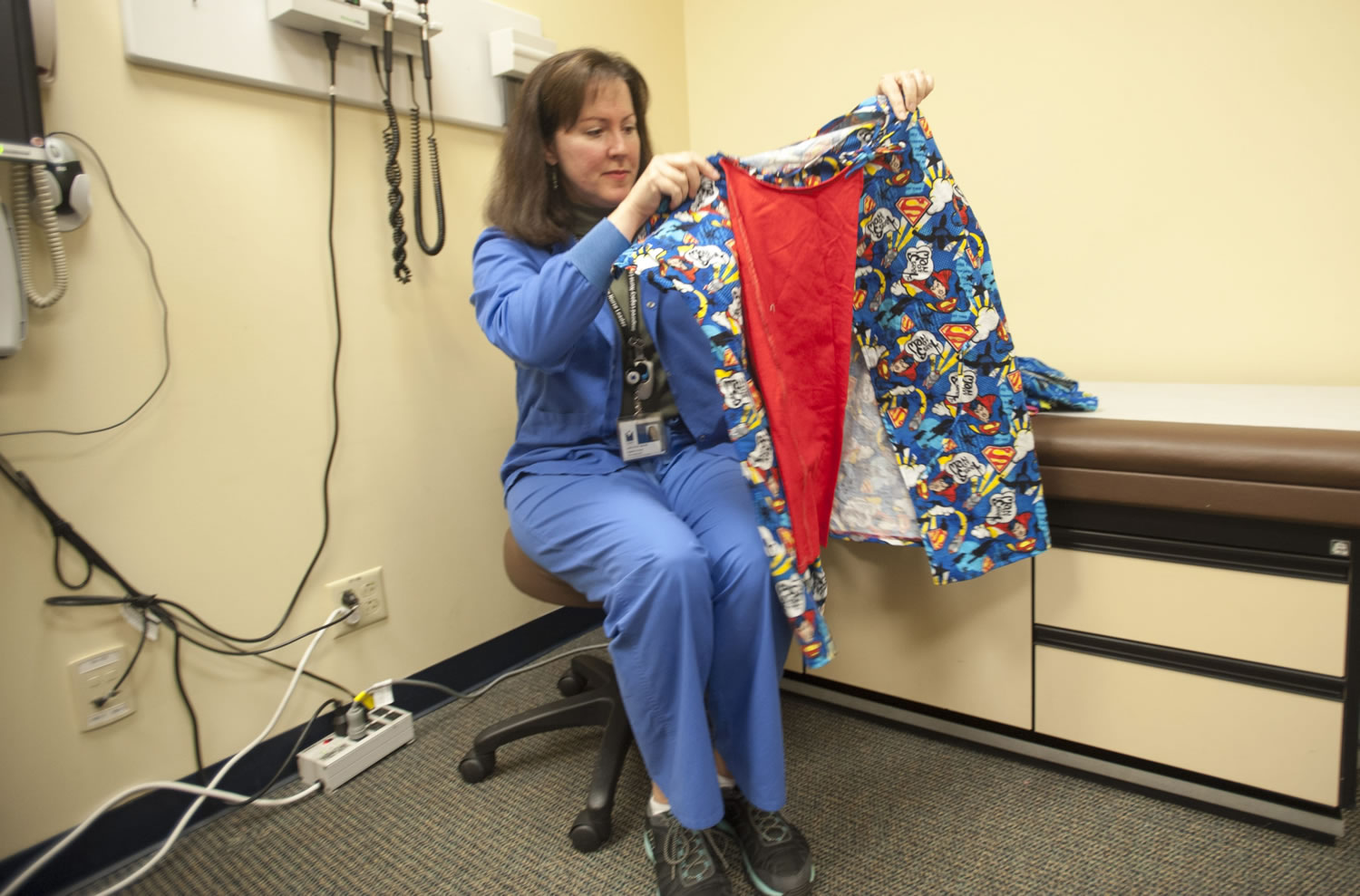 Charge nurse Carolyn Wynne shows off a superhero-themed gown she helped create for children who have to undergo physical exams through the Child Abuse Assessment Team.