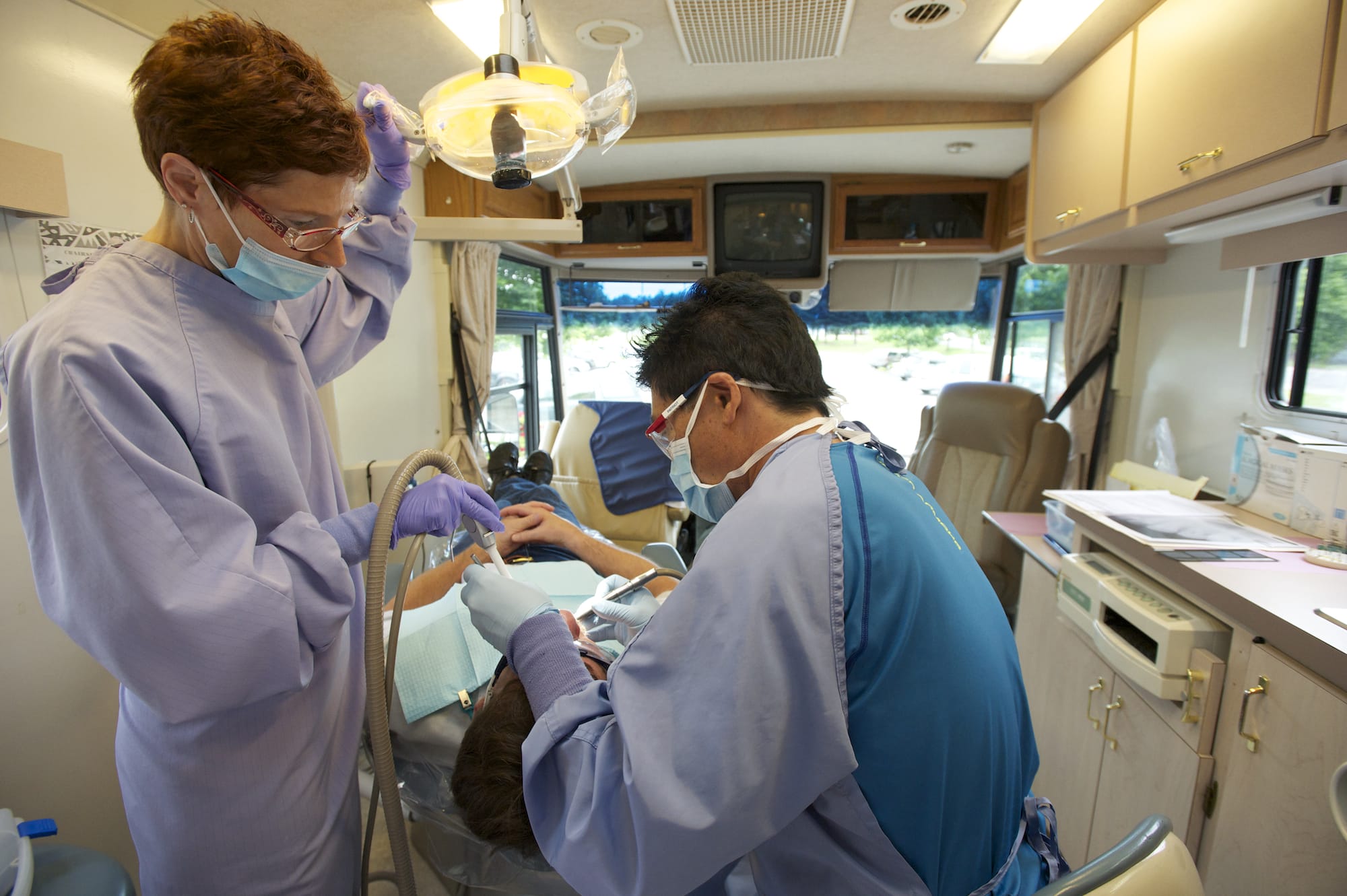 Dentist Martin Hikido, right, and dental assistant Terri Erickson tend to patient Randy Hash in a dental van.
