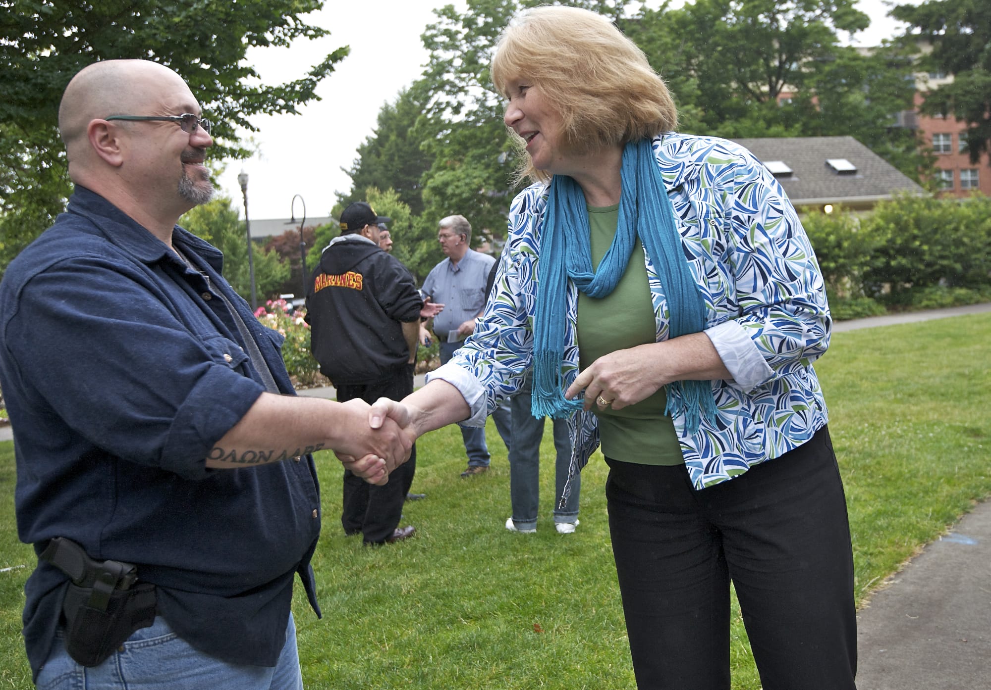 Open-carry gun activist Larry White and gun safety advocate and Vancouver City Councilwoman Anne McEnerny-Ogle shake hands as the two groups hold their separate rallies at Esther Short Park on Tuesday. McEnerny-Ogle was one of the few people who crossed camps to interact with the other group.