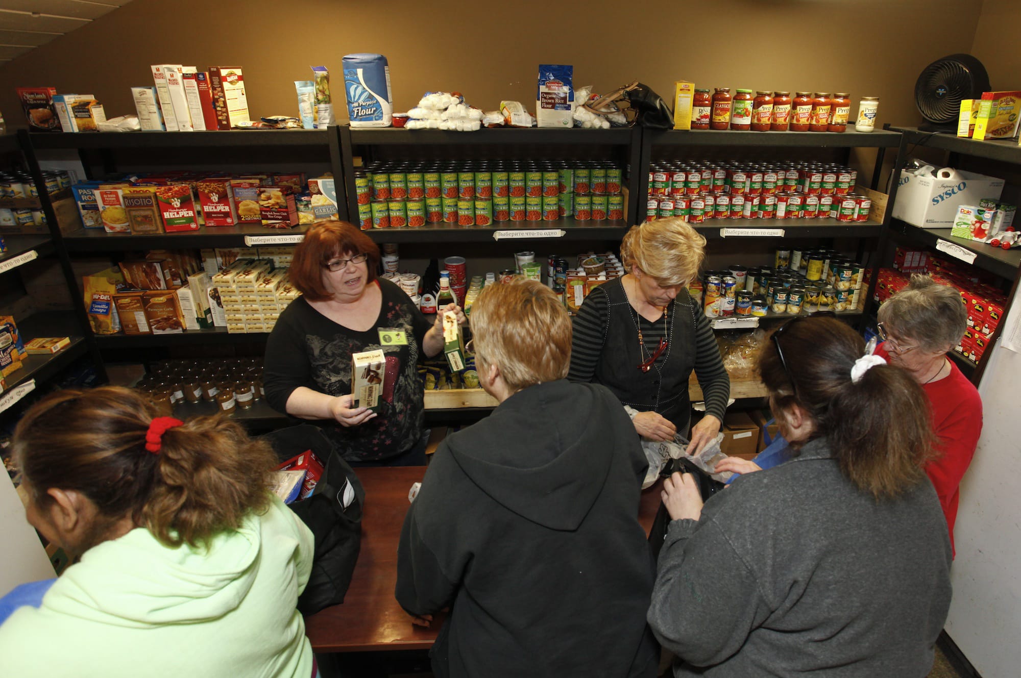 Volunteers Susie Riser, left, and Susan Stoval distribute grocery items to a capacity crowd at the SixEight food pantry in Hazel Dell.