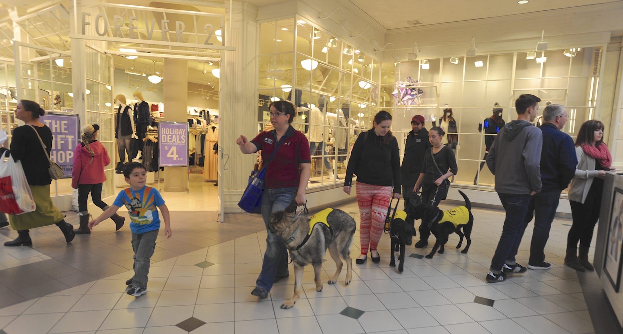 Becca Khalil, center, with her son Adrian, at left, leads Izaac, a service dog in training, during an exercise earlier this month at Westfield Vancouver mall.