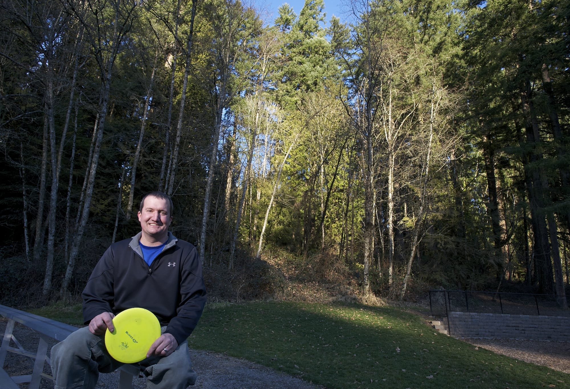 Mike Nemeth, who serves on Ridgefield's parks board and is the project lead in efforts to develop a disc golf course at Ridgefield's Abrams Park, sits near the wooded embankment where the course is proposed.