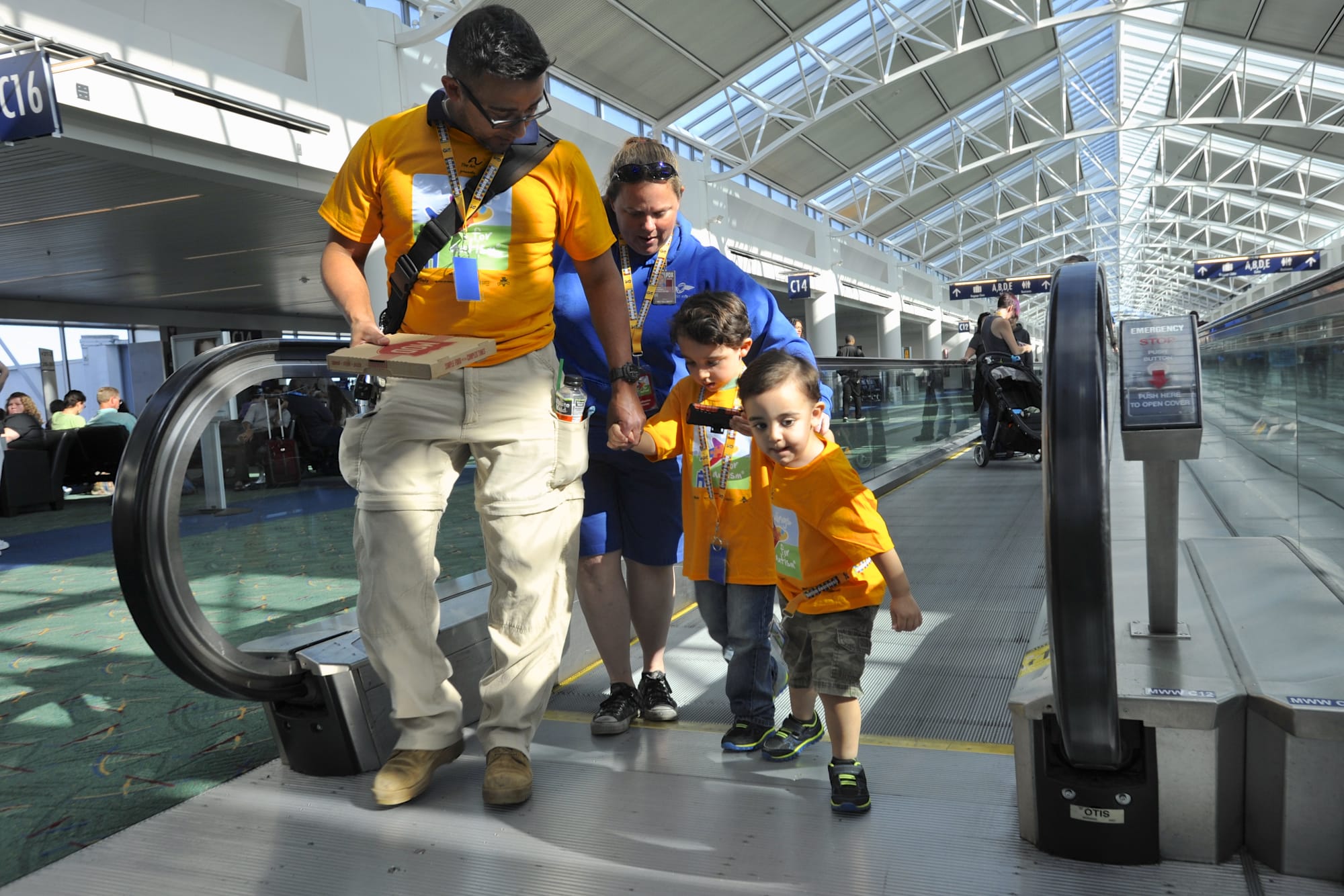Saul Martinez Class, left, assists Owen Martinez with Catharine Hunter and Joshua Martinez, right, on the moving walkway at PDX at an event where families with children with autism could practice boarding a plane.