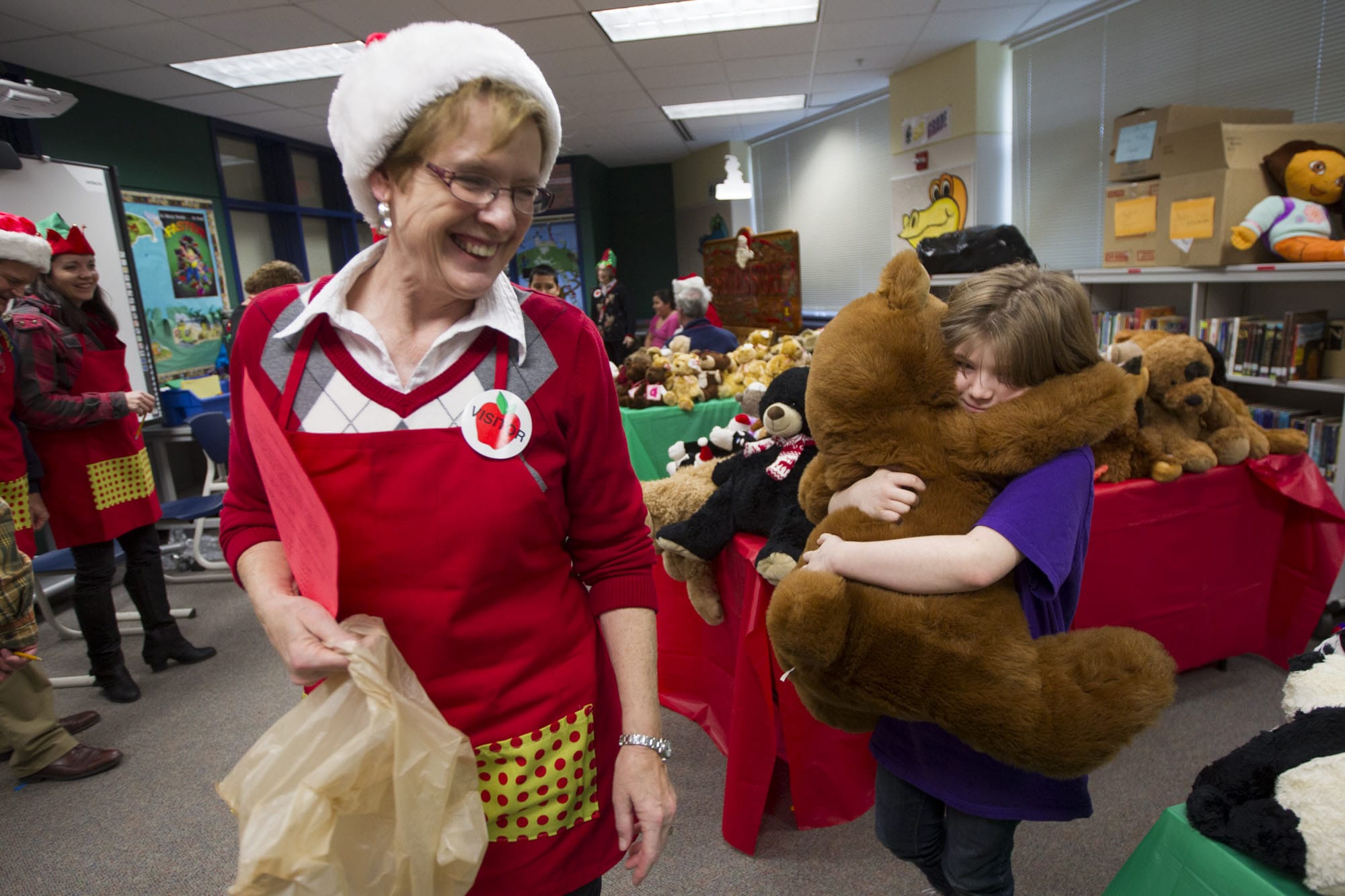 Fifth-grader Amy Shook hugs a stuffed bear as volunteer Renee Rhyasen helps her shop for gifts at Washington Elementary on Thursday.