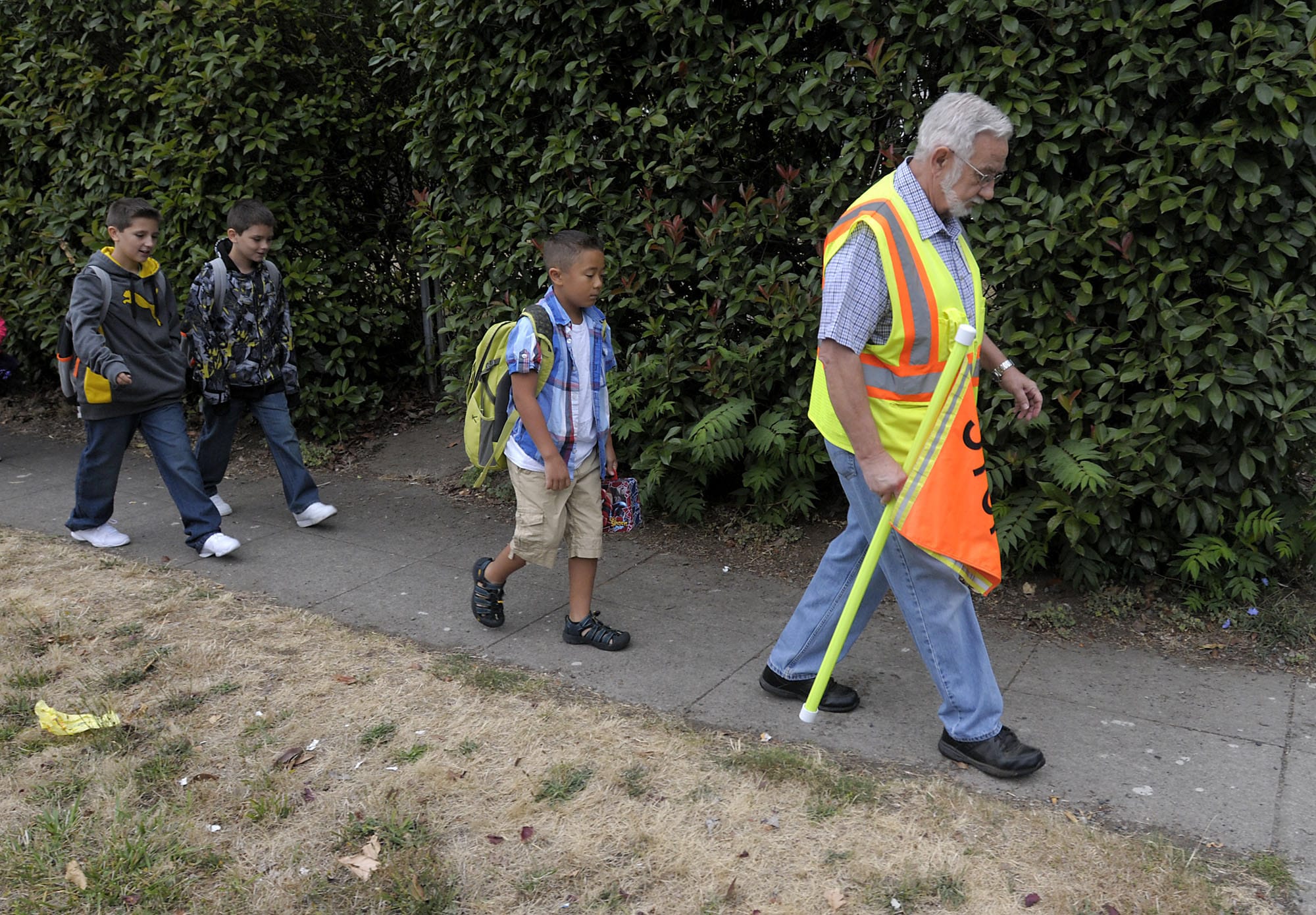 Volunteer Mick Hawthorn escorts Trevor Watts, his brother Owen and Aderris Bantilan, from left, to Washington Elementary via East 33rd Street on Wednesday morning.