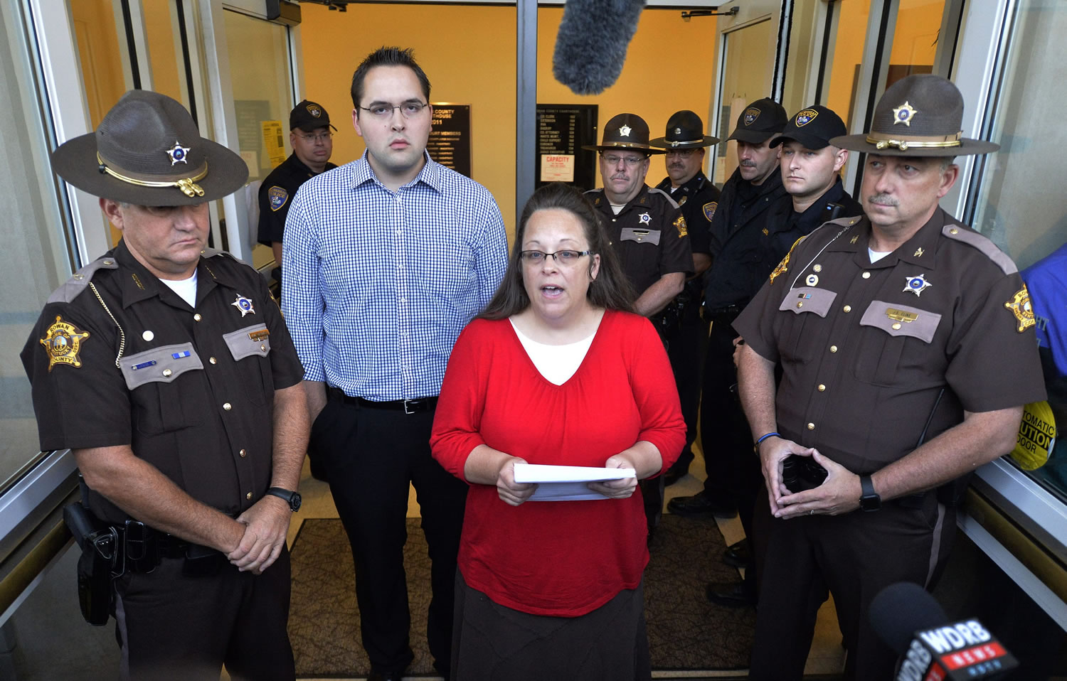 Surrounded by Rowan County Sheriff's deputies, Rowan County Clerk Kim Davis, center, with her son Nathan Davis standing by her side, makes a statement to the media at the front door of the Rowan County Judicial Center in Morehead, Ky., on Monday. Davis announced that her office will issue marriage licenses under order of a federal judge, but they will not have her name or office listed. (AP Photo/Timothy D.