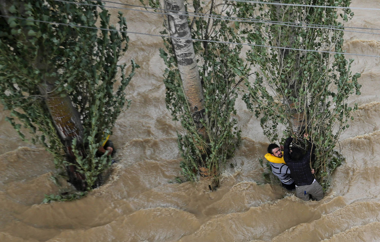 Kashmiris hang on to a tree to prevent being swept away by floodwaters in Srinagar, India, Tuesday, Sept. 9, 2014. The death toll from floods in Pakistan and India reached 400 on Tuesday and have put more than half a million people in peril and rendered thousands homeless in the two neighboring states.