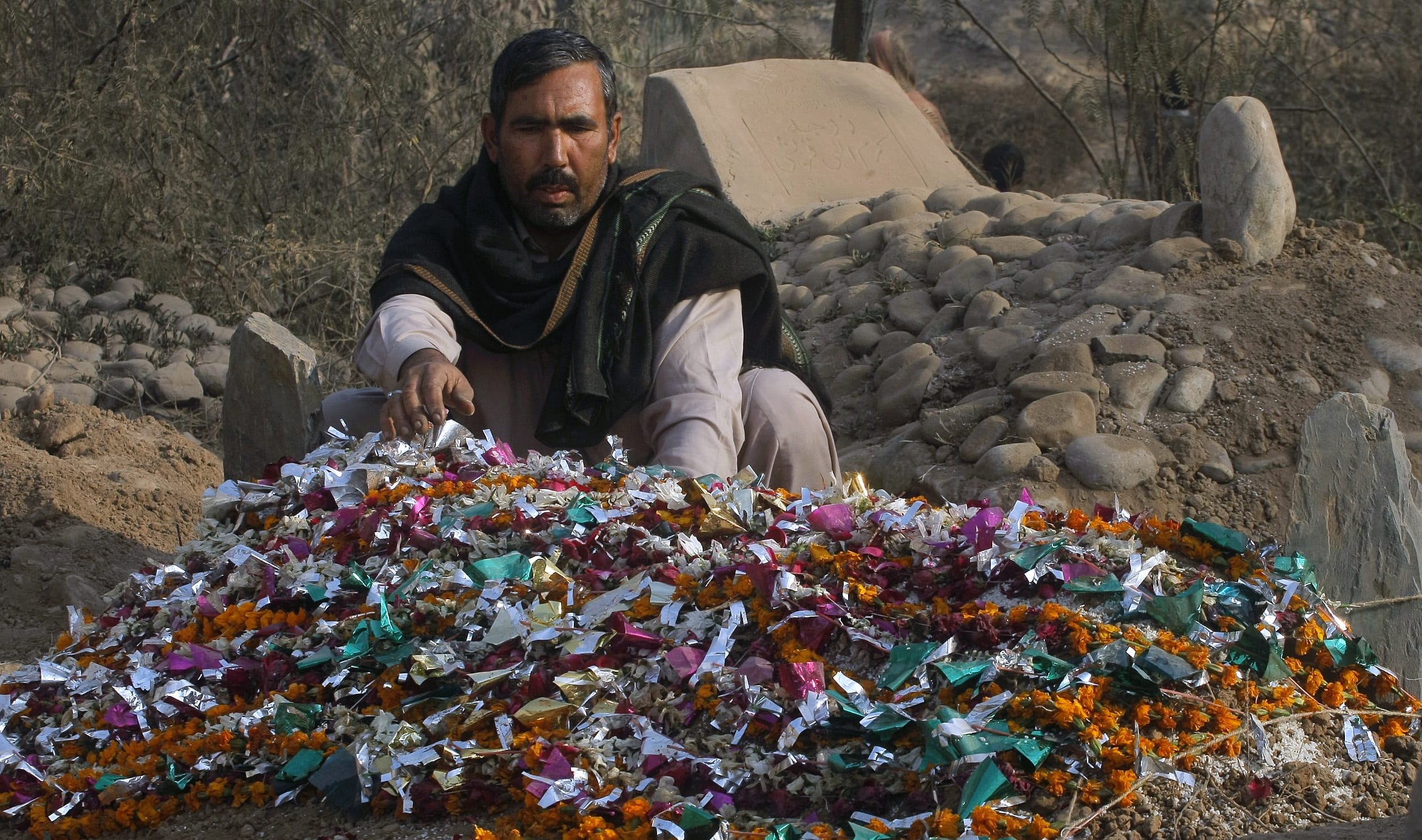Pakistani gravedigger Taj Muhammad adjusts wreaths on a grave Saturday at the Rahman Baba graveyard in Peshawar, Pakistan.