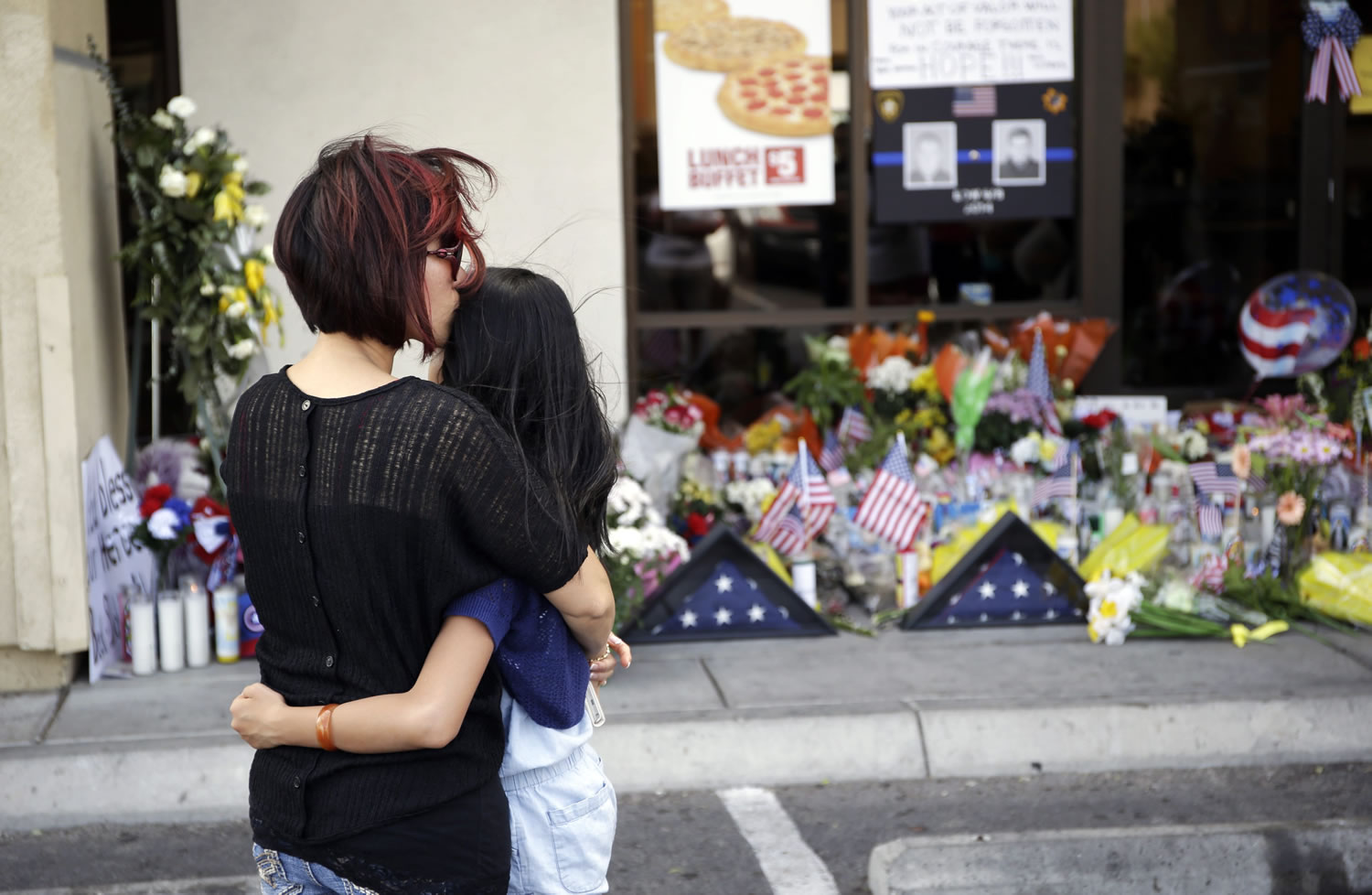 Hieu Le kisses her 9-year-old daughter Allie Le on Tuesday while visiting a makeshift memorial at a CiCi's Pizza in Las Vegas, where a Sunday attack killed police officers Alyn Beck, 41, and Igor Soldo, 31.