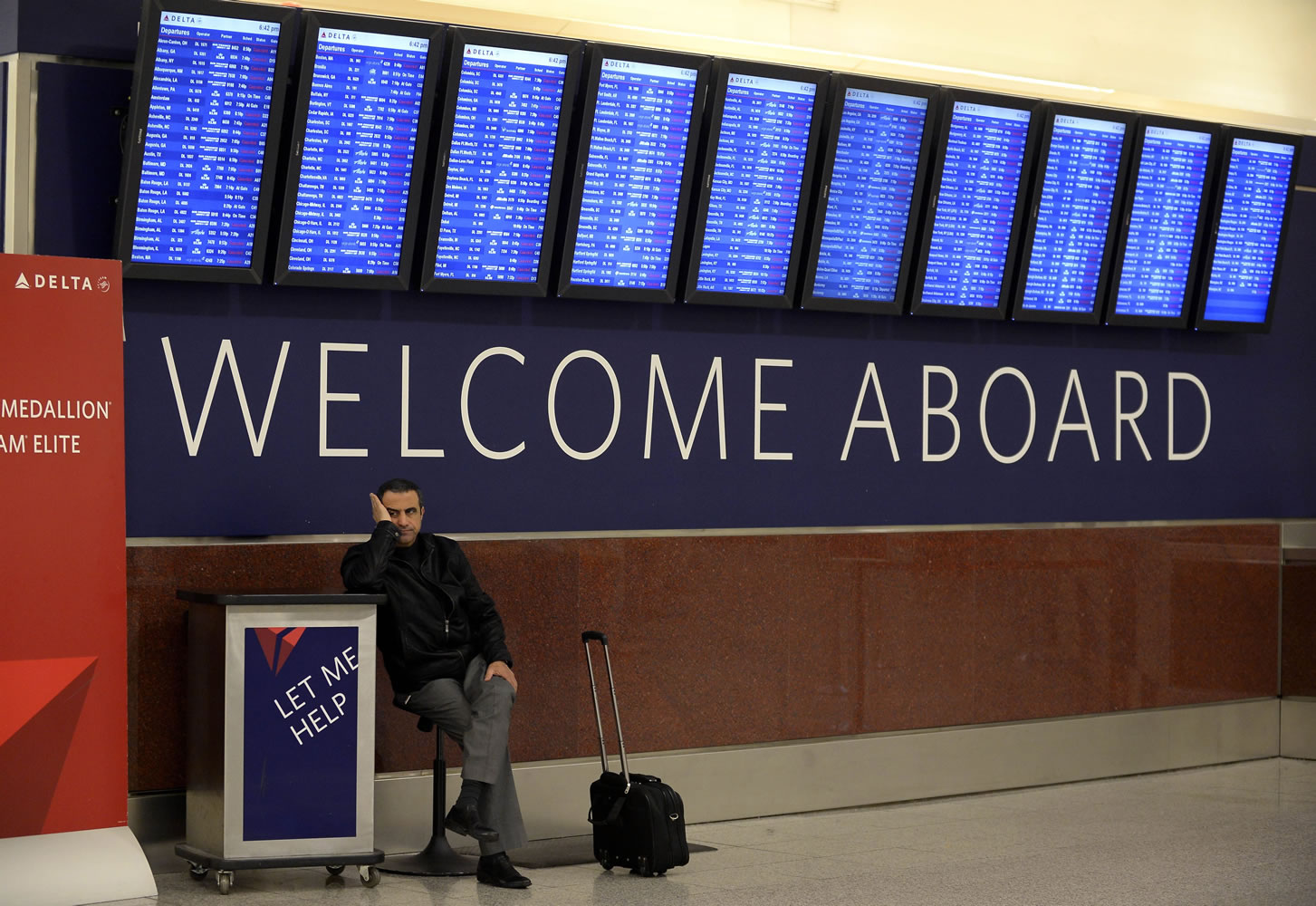 An airline passenger waits for his rescheduled flight to Orlando under the departure board showing hundreds of cancellations at Hartsfield-Jackson International Airport in Atlanta.