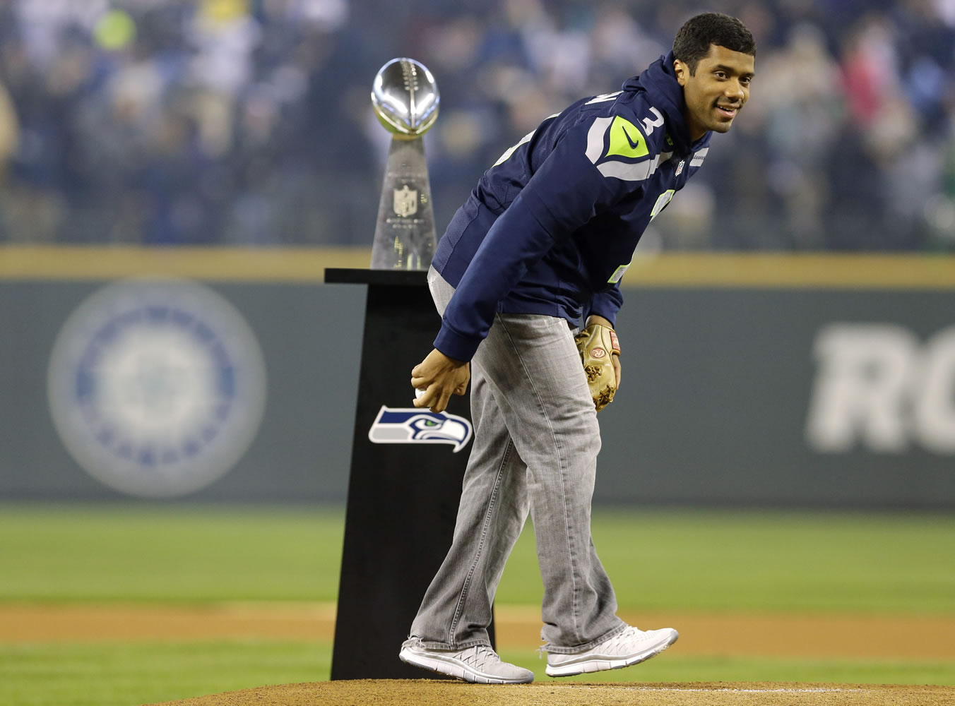 Seattle Seahawks quarterback Russell Wilson stands by the Vince Lombardi Trophy as he winds up to throw the ceremonial first pitch Tuesday at the Seattle Mariners' baseball home-opener.