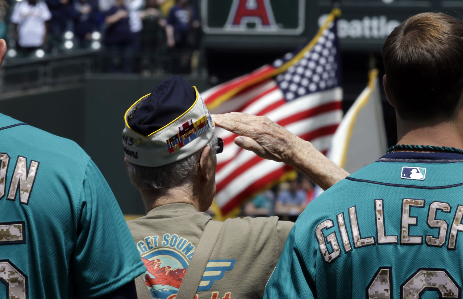 Veteran Ralph Laedtke, of Washougal, stands between Seattle Mariners players as he salutes during the national anthem before Monday's game at Safeco Field. Veterans were honored before the game in recognition of Memorial Day.