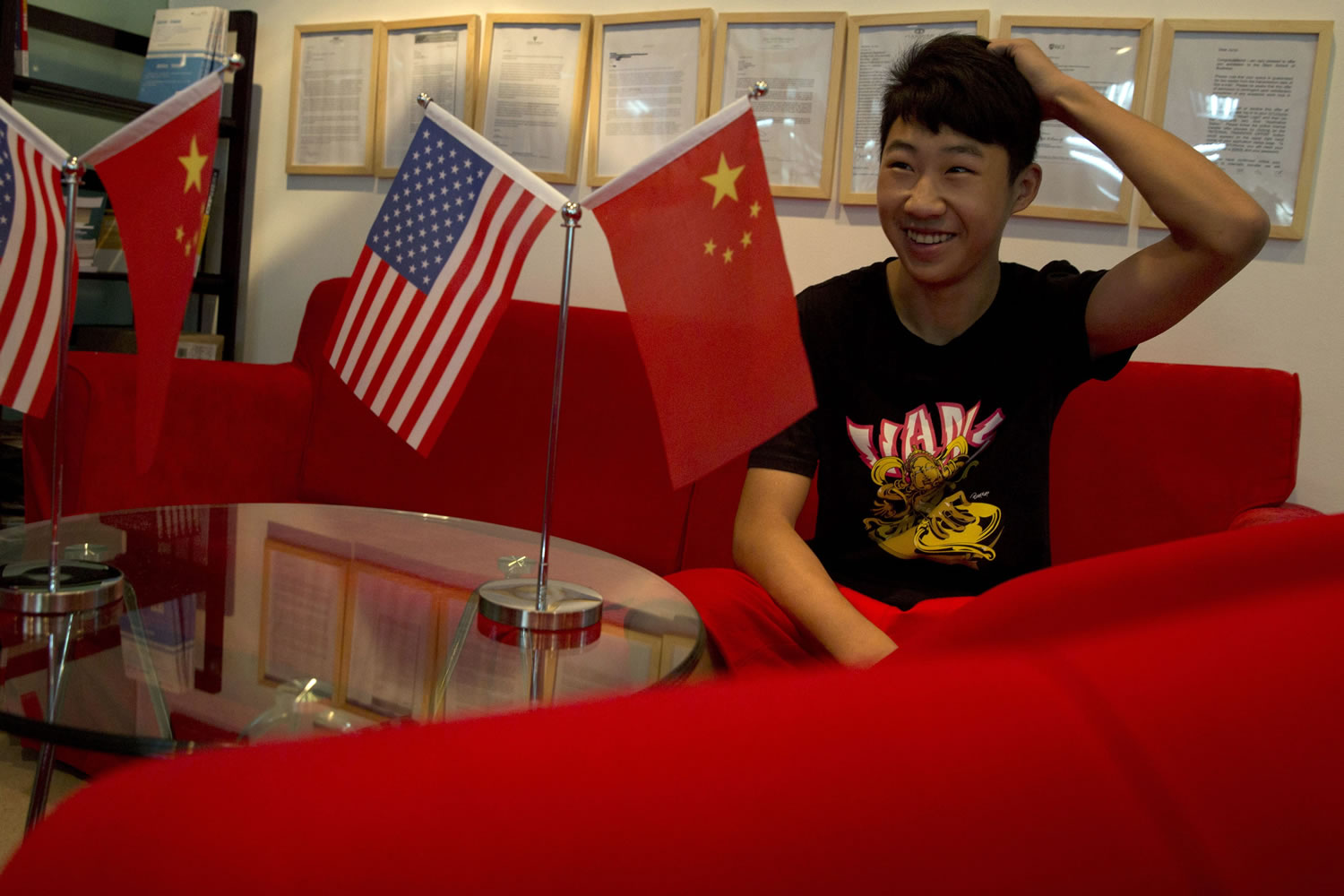 Zhang Kaisheng, 16, sits last month in the lobby of Focus Education, a tutoring and consulting agency in Beijing, decorated with national flags of China and the U.S.  Zhang plans to enroll this fall in a private U.S.