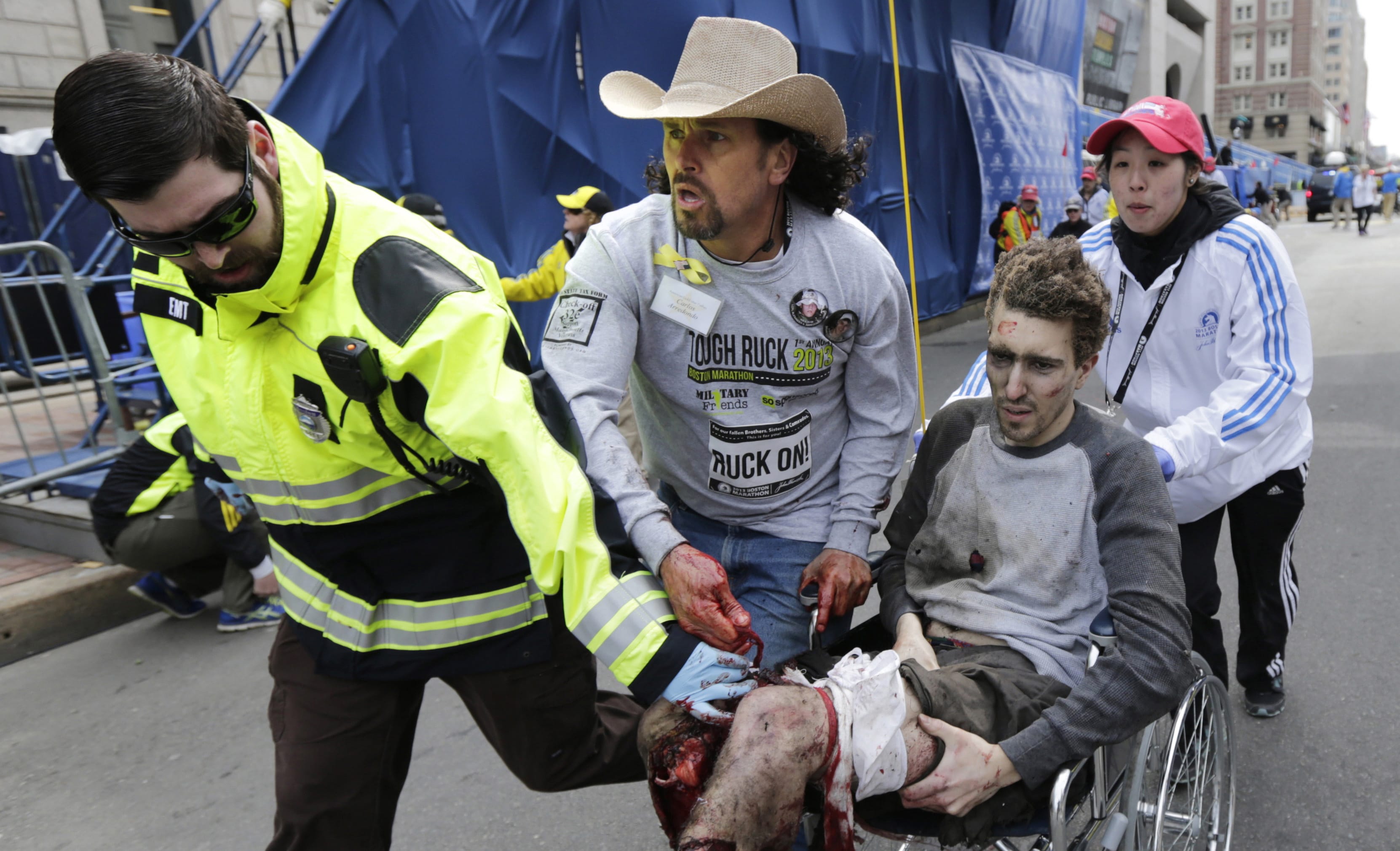 Boston EMT Paul Mitchell, left, bystander Carlos Arredondo, in cowboy hat, and Boston University student Devin Wang push Jeff Bauman in a wheelchair after he was injured in last year's Boston Marathon bombing.
