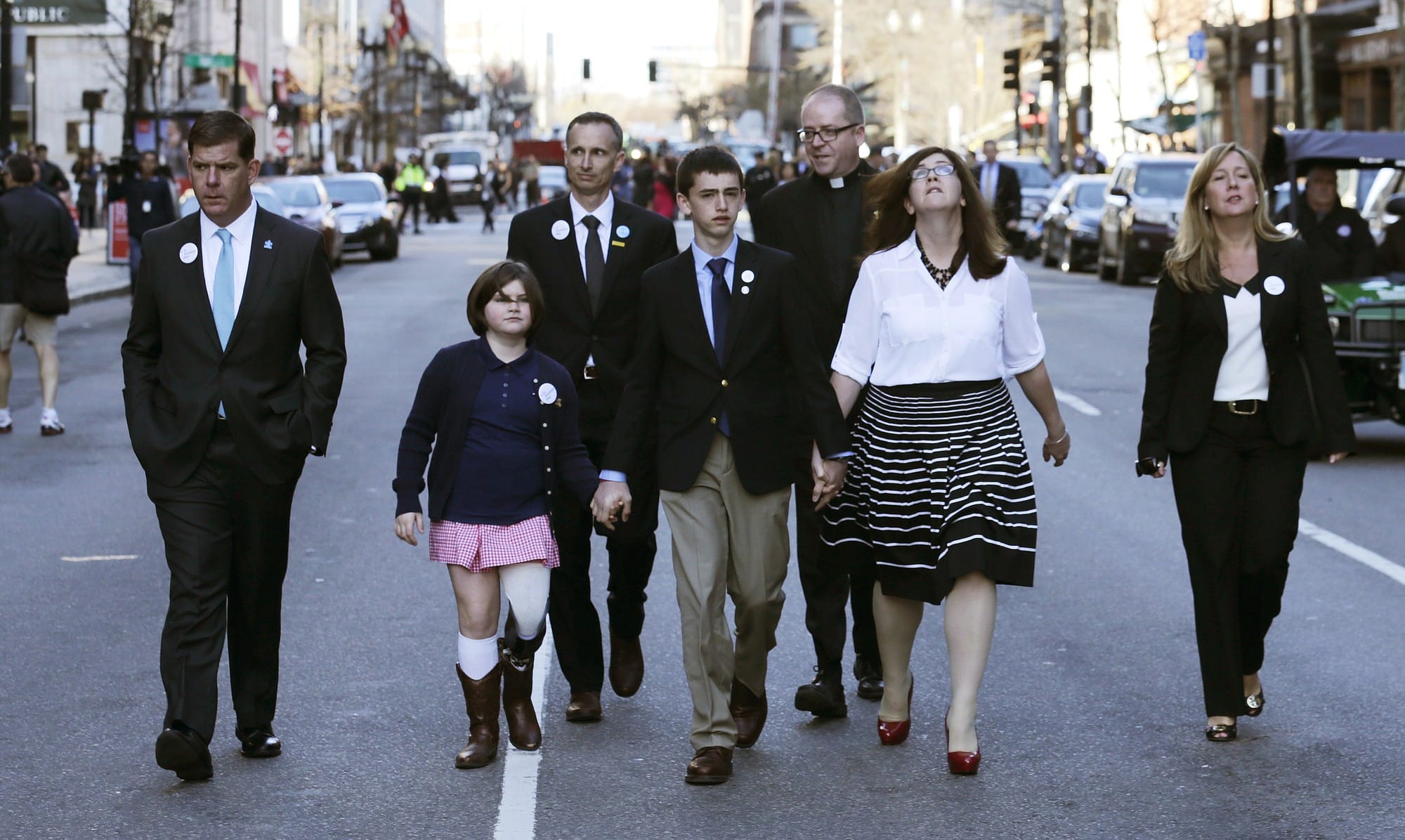 Boston Marathon survivor Jane Richard, who has a prosthetic left leg, holds the hand of her brother Henry, center, as their family walks down Boylston Street with Boston Mayor Marty Walsh, left, after a ceremony Wednesday honoring victims and survivors at one of two blast sites near the finish line of the Boston Marathon.
