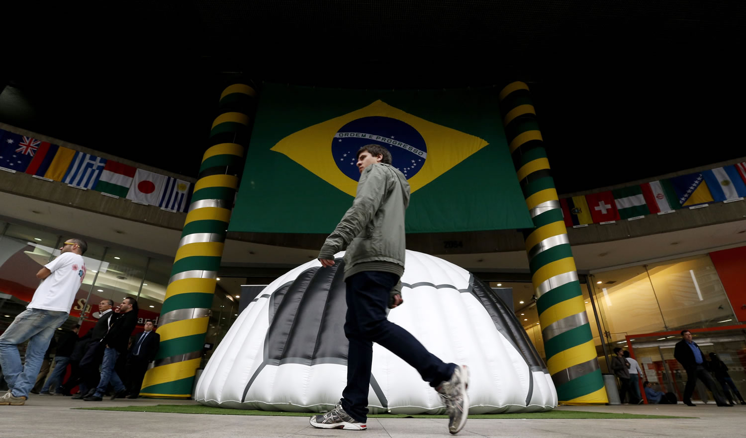 A man walks near a shopping center where a large Brazil flag and half of a soccer ball decorate the entrance in Sao Paulo, Brazil, Tuesday, June 10, 2014. The World Cup is set to open on June 12 with Brazil facing Croatia in Sao Paulo.