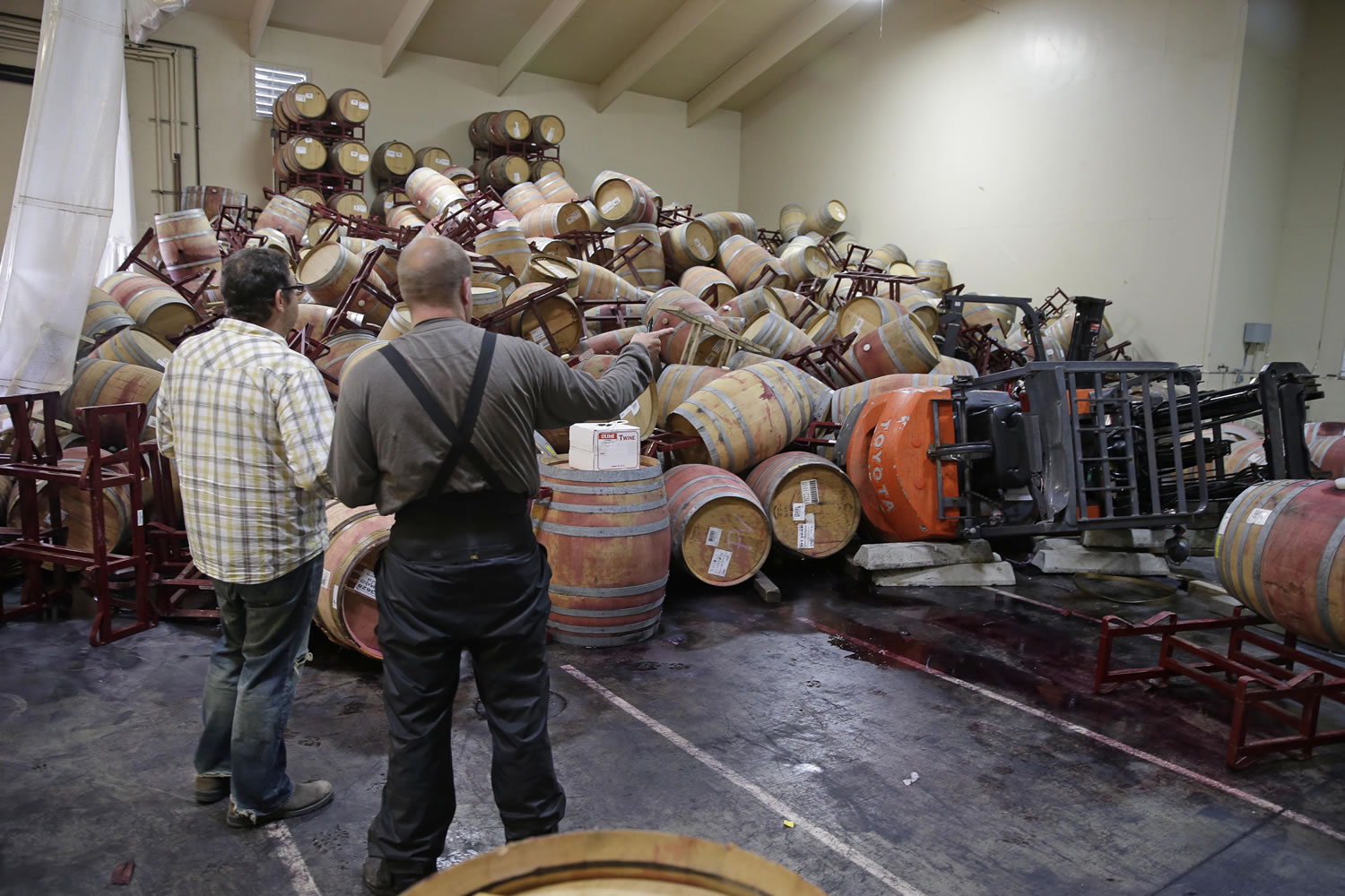 Jeremy Weiss, left, and cellar worker Adam Craig, right, look over some of the hundreds of earthquake damaged wine barrels that covered and toppled a pair of forklifts at the Kieu Hoang Winery on Monday in Napa, Calif.