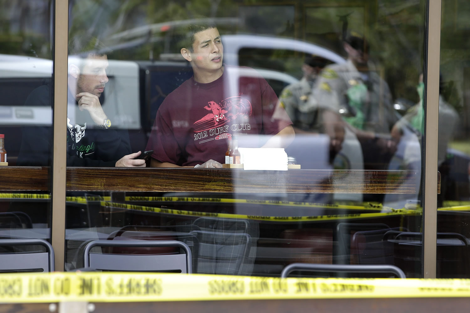 Two men watch from a restaurant near the scene of a shooting on Saturday in Isla Vista, Calif.