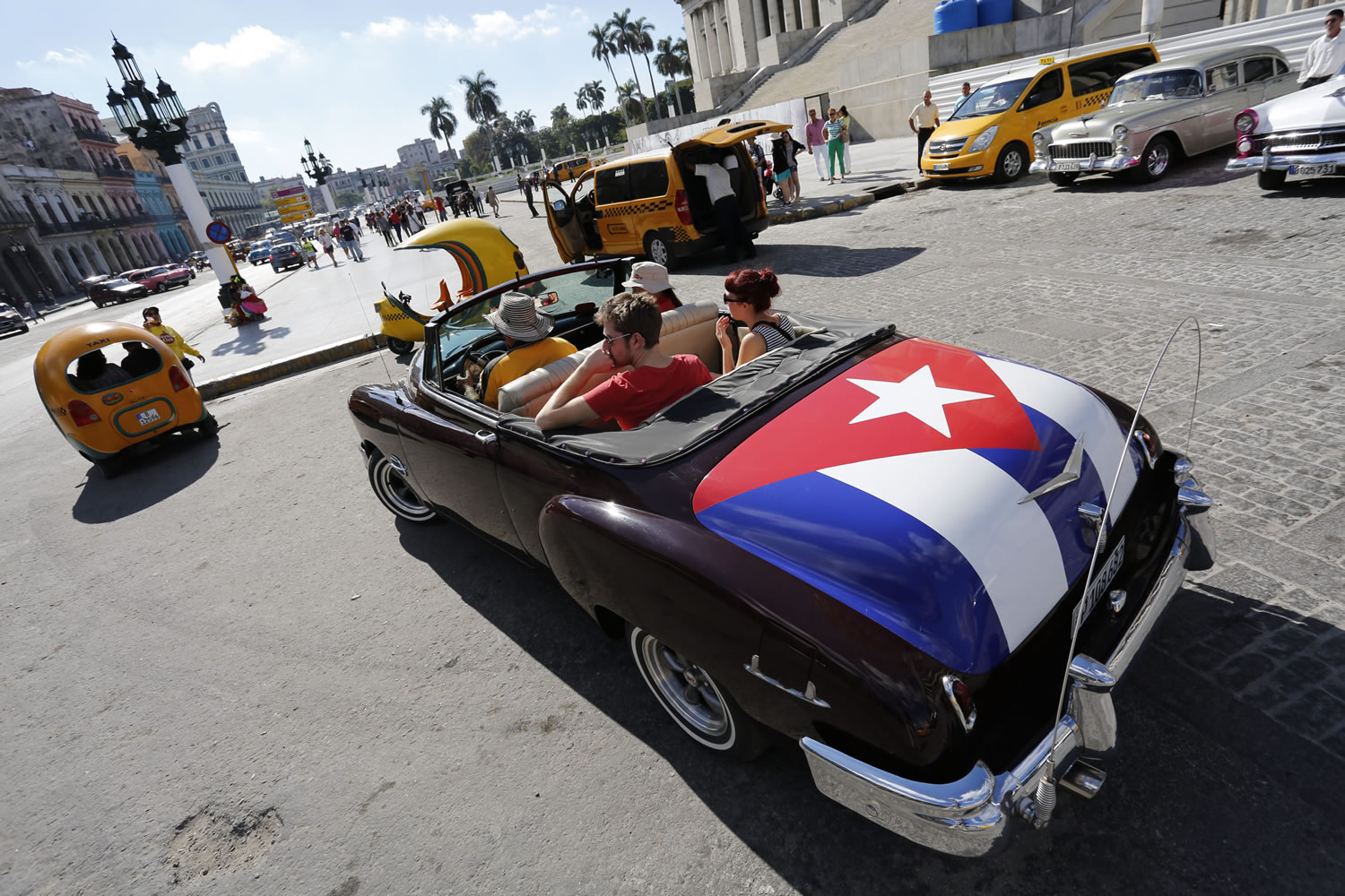 Tourists take a ride in a classic American car with the Cuban national flag painted on the trunk Thursday in Havana, Cuba.