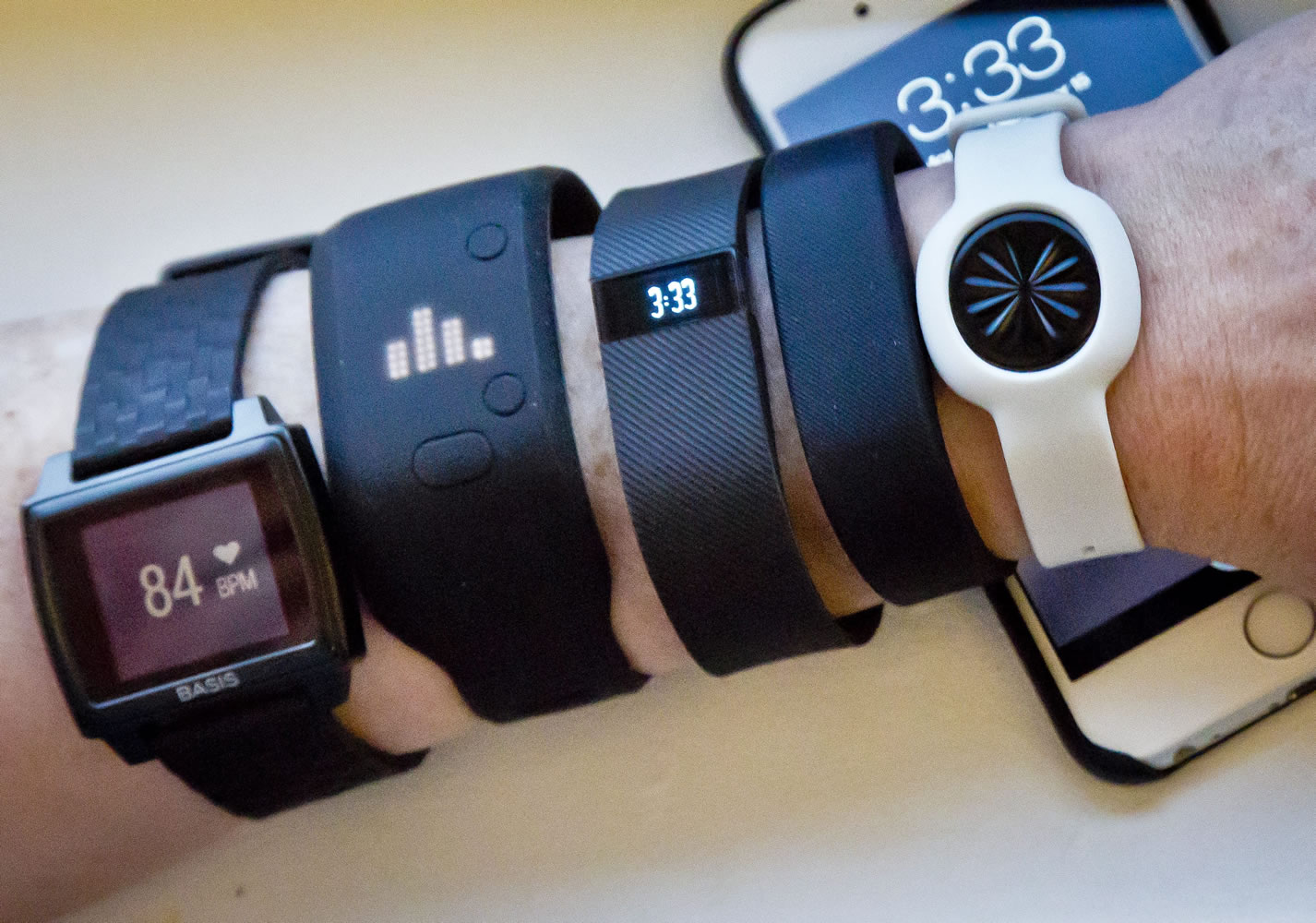 Fitness trackers, from left, Basis Peak, Adidas Fit Smart, Fitbit Charge, Sony SmartBand, and Jawbone Move, are displayed, with an iPhone in the background.