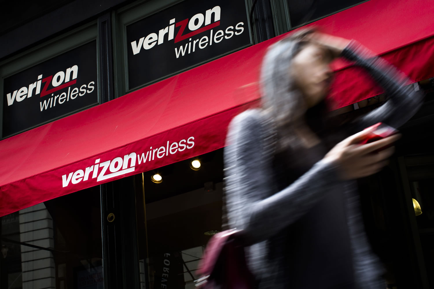 A pedestrian uses her cell phone as she passes a Verizon Wireless store on Broadway in Lower Manhattan in New York.