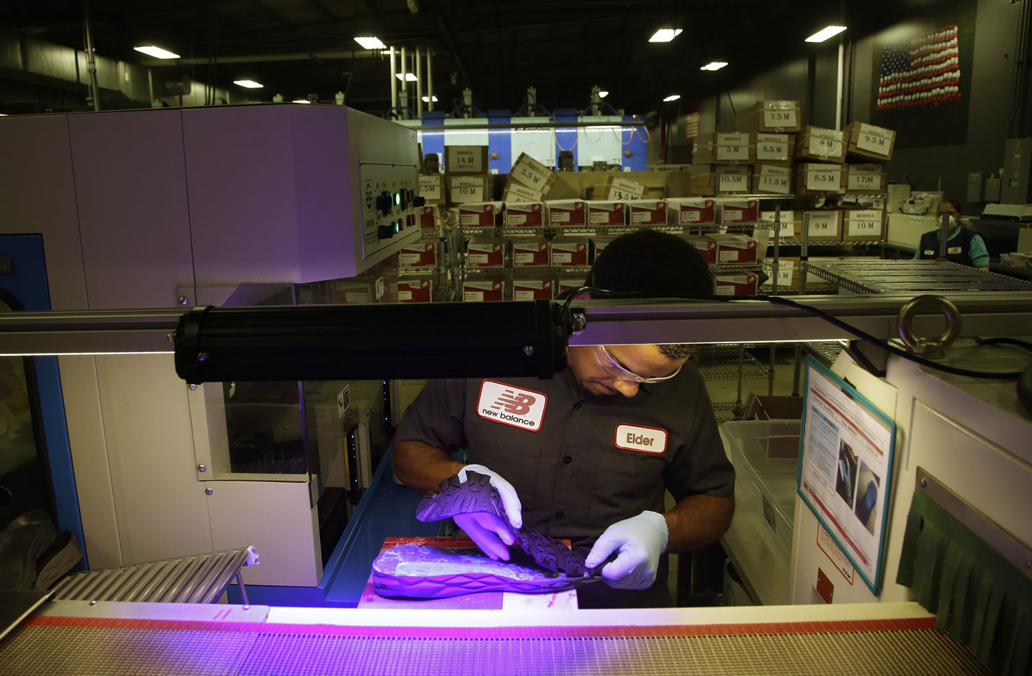 Elder Brandao, working under ultraviolet lights, glues an outsole to a midsole of the New Balance proposed 950v2 sneaker, that has passed military testing, at one of company's manufacturing facilities in Boston.