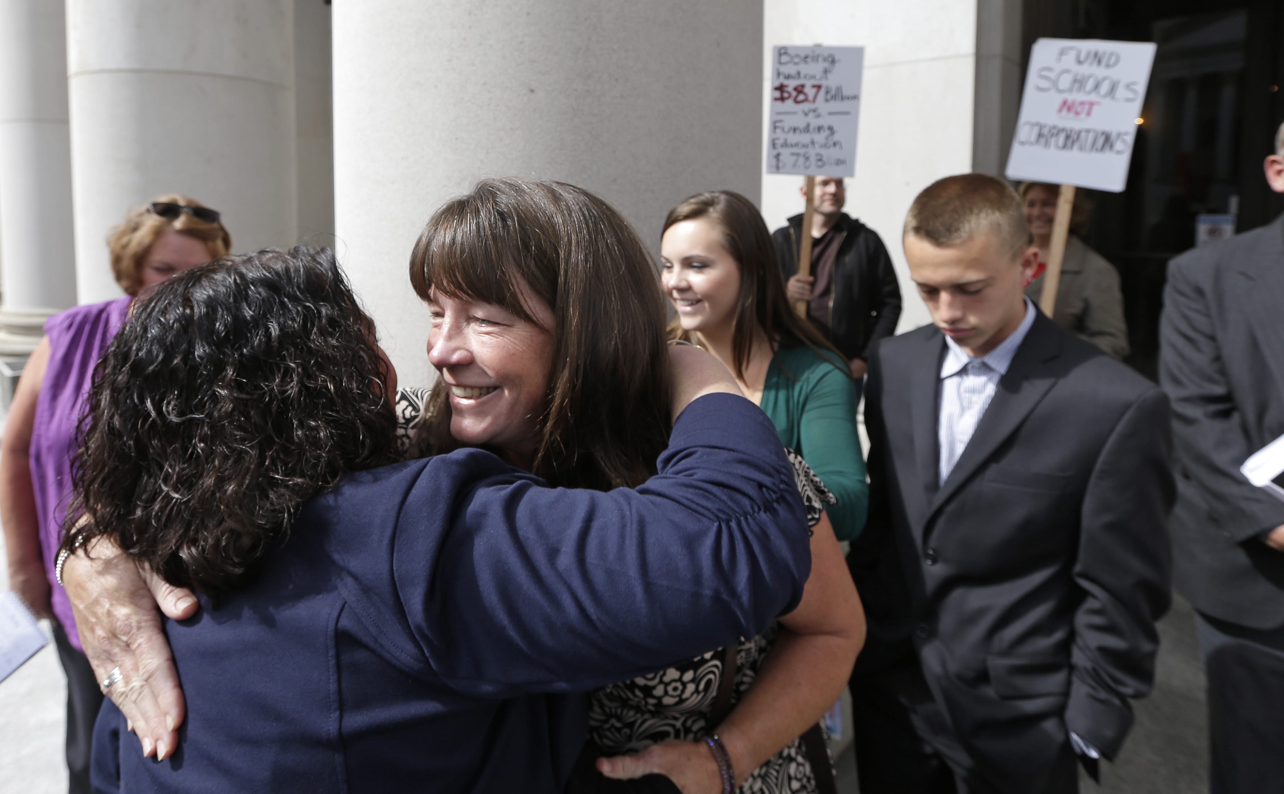 Plaintiff Stephanie McCleary, with her children Kelsey, 20, and Carter, 15, right, behind, is embraced outside following a Sept. 3 hearing before the state Supreme Court in Olympia.