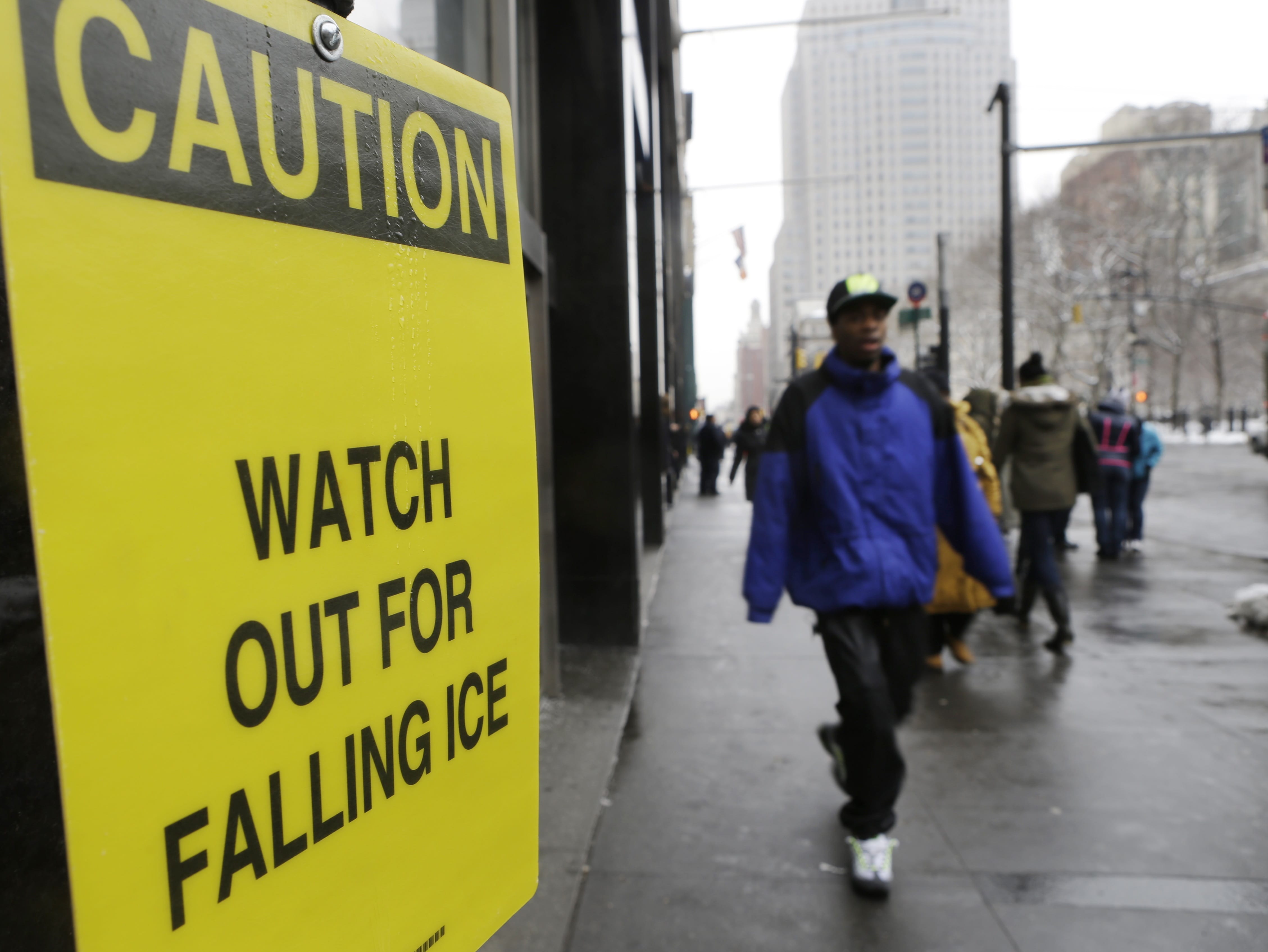 Pedestrians pass a sign warning them of falling ice near City Hall Tuesday in New York.