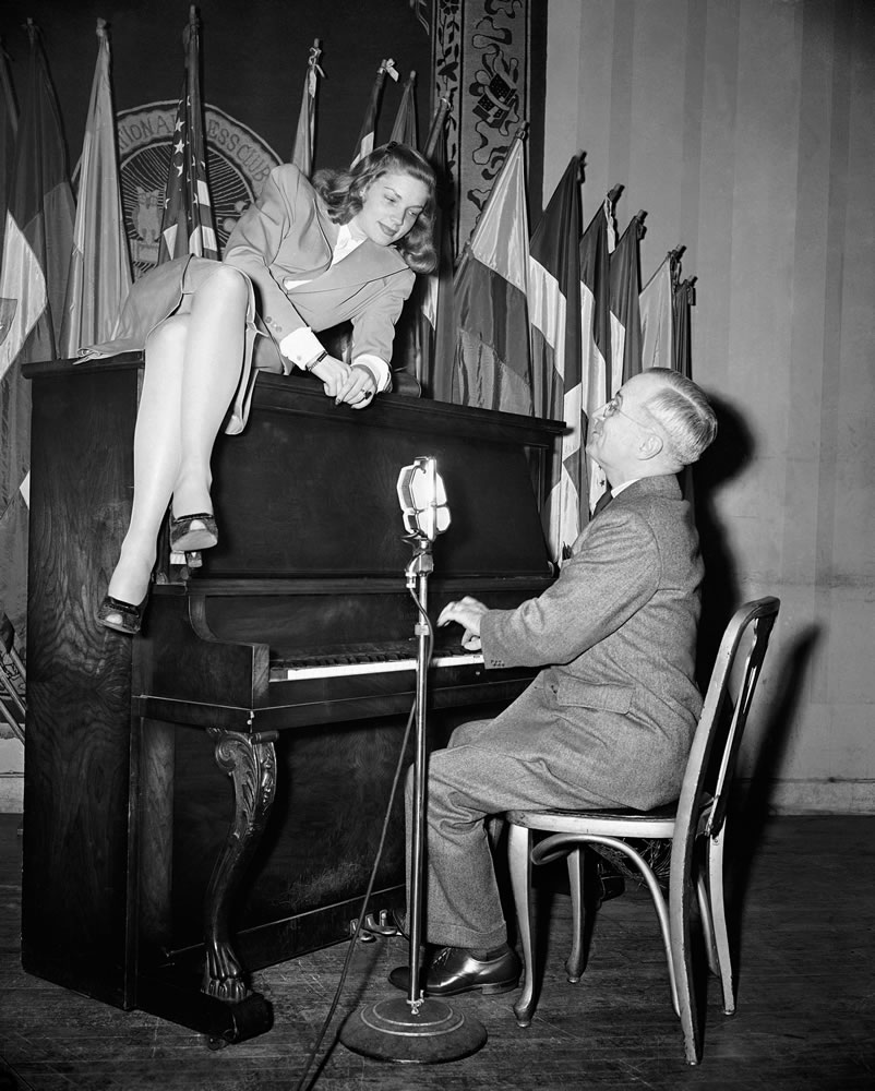 FILE - In this Feb. 10, 1945 file photo, Vice President Harry S. Truman plays the piano as actress Lauren Bacall lies on top of it during her appearance at the National Press Club canteen in Washington. Bacall, who died Tuesday, Aug.12, 2014, at 89, was a fashion darling of a unique sort. A model at 16, later a pal of Yves Saint Laurent and a frequent wearer of designs by Norman Norell.