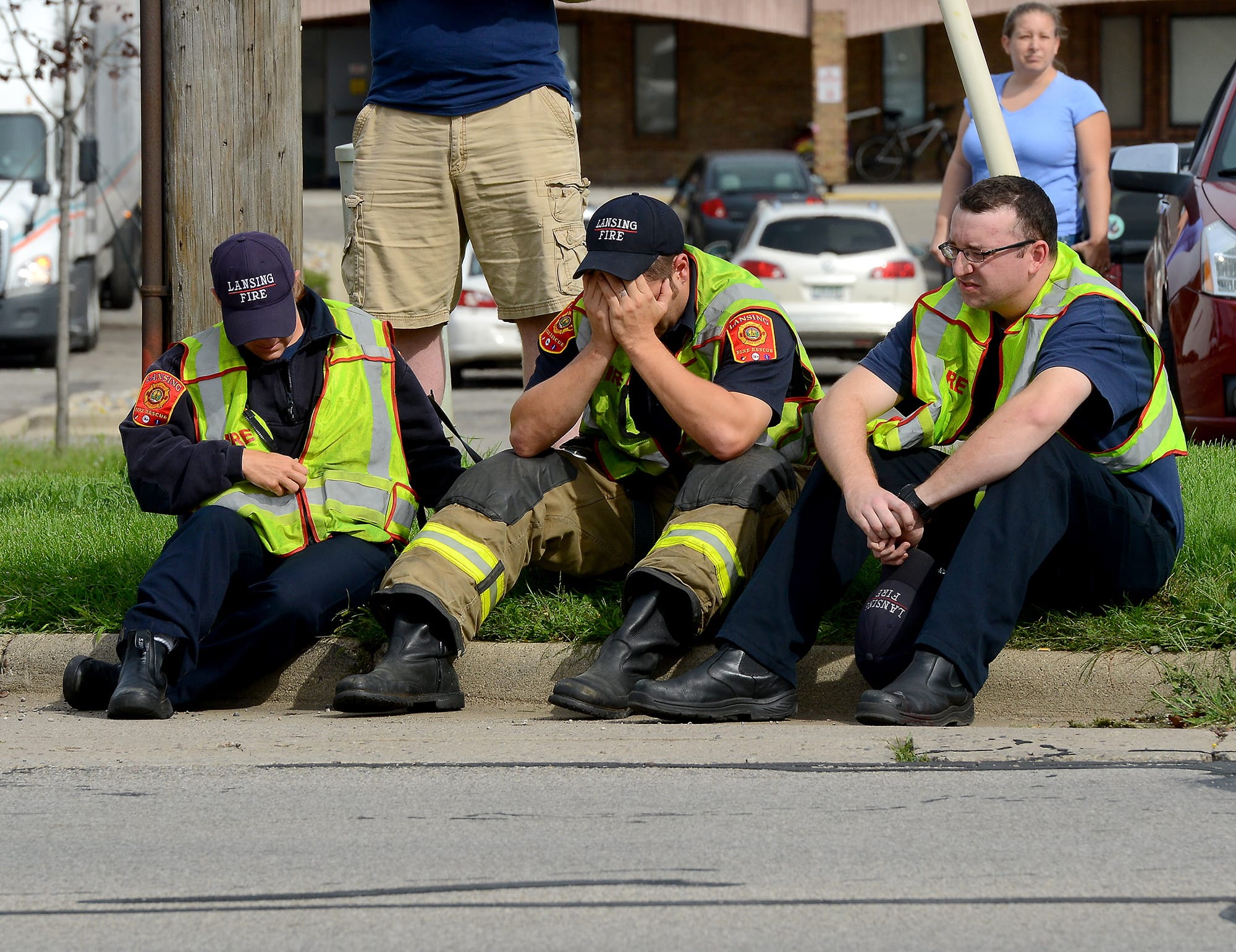 A firefighter puts his head in his hands as he and other firefighters sit on the curb on Cedar Street just north of Jolly Road on Wednesday in Lansing, Mich. Dennis Rodeman, a 35-year-old Lansing firefighter has died after being struck by a hit-and-run driver as he collected money for charity.