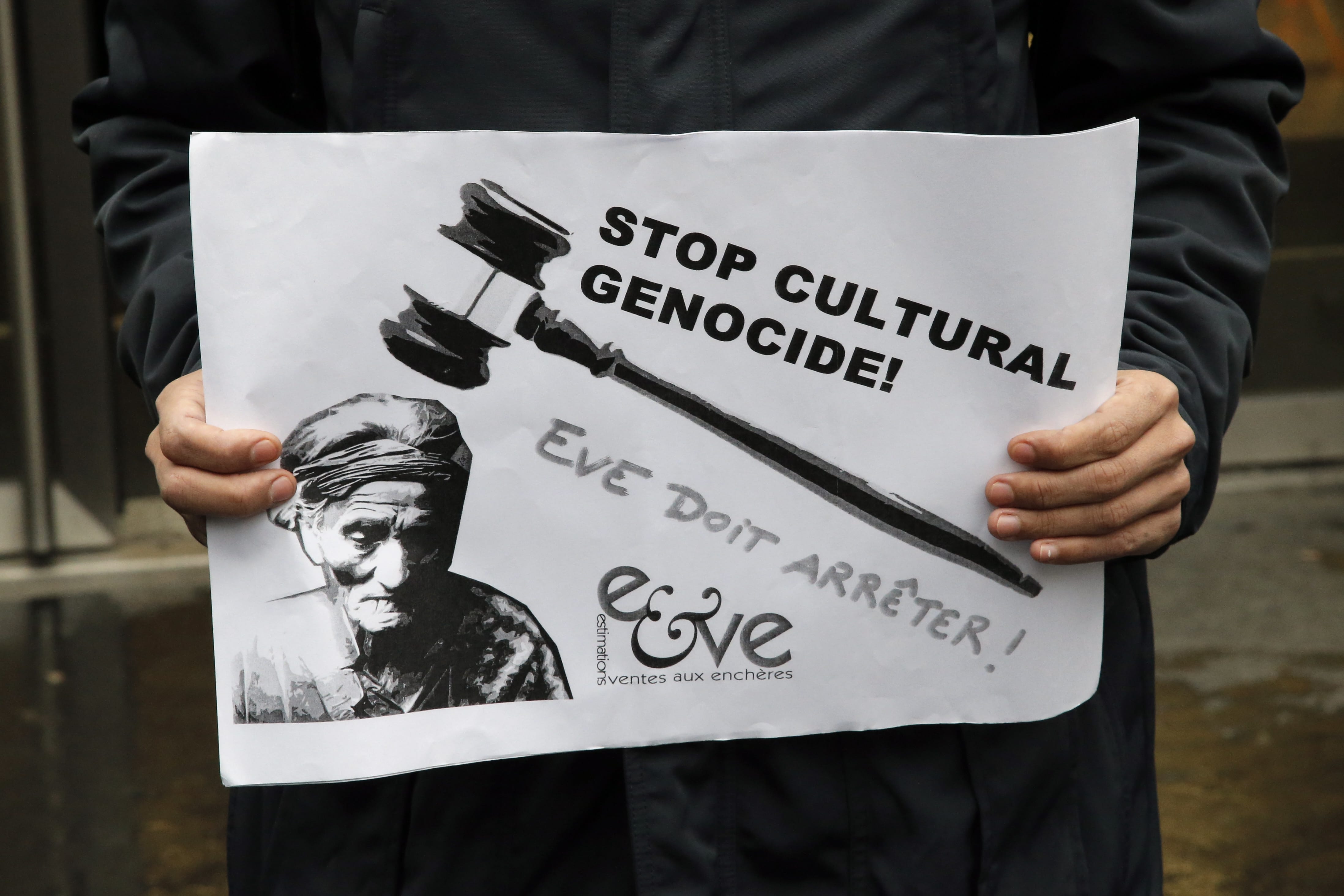 A supporter of Native Americans holds a leaflet reading &quot;Stop cultural genocide, Eve auction house must stop&quot; to protest outside of the Drouot's auction house during the contested auction of Native American items in Paris on Monday.