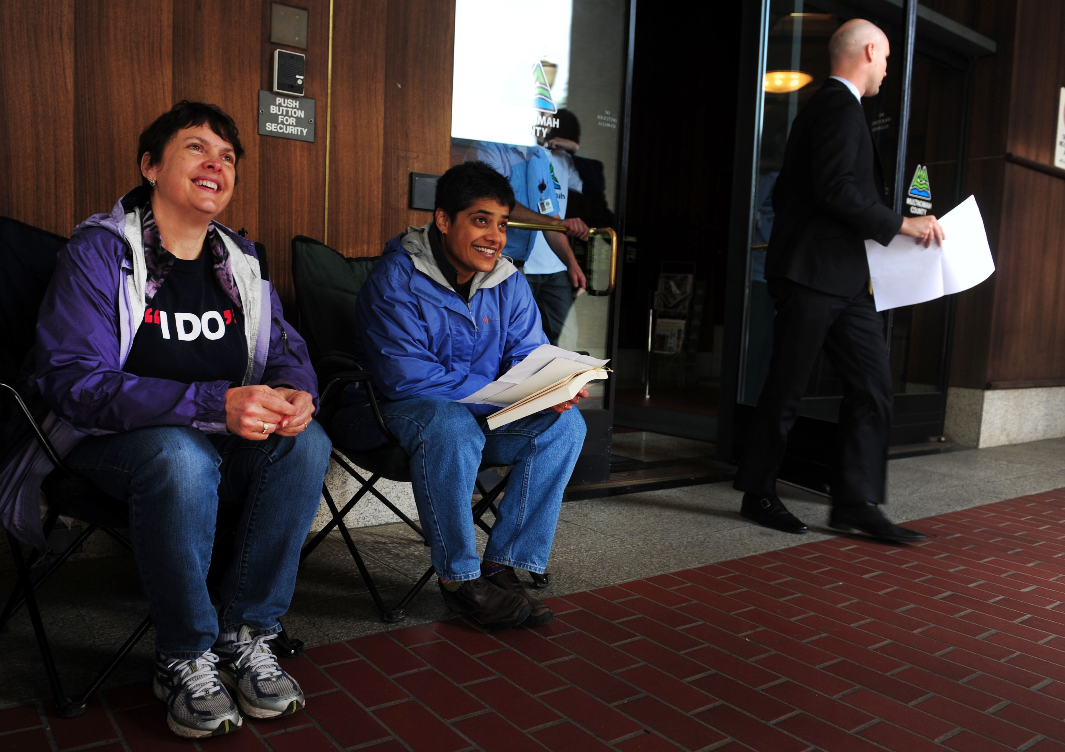 Laurel Gregory, left, and Shilpi Benerjee pass the time in front of the Multnomah County Recorder's building in Portland on Monday.