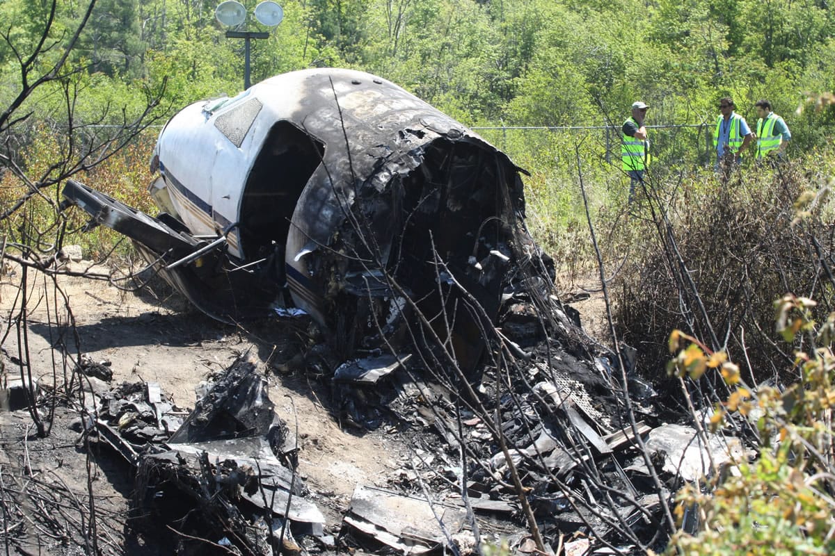 Officials work near wreckage at the scene Monday in Bedford, Mass., where a plane plunged down an embankment and erupted in flames during a takeoff attempt at Hanscom Field on Saturday night.
