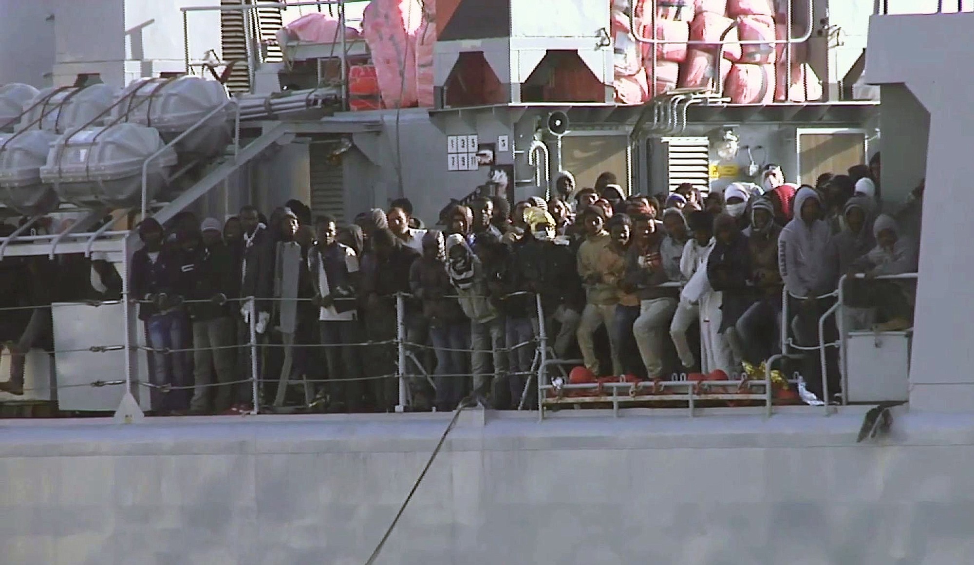 In this image from TV, migrants crowd at the rail aboard an Italian navy vessel as it cruises toward the Italian port of Messina on Saturday.