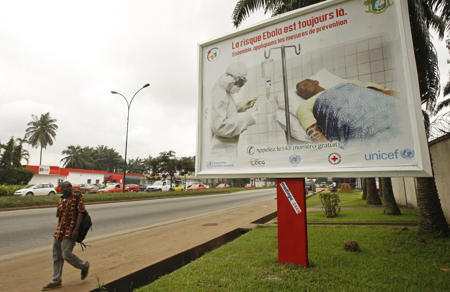 A man, left, walk past a Ebola awareness campaign poster, in the city of Abidjan, Ivory Coast, on Monday.