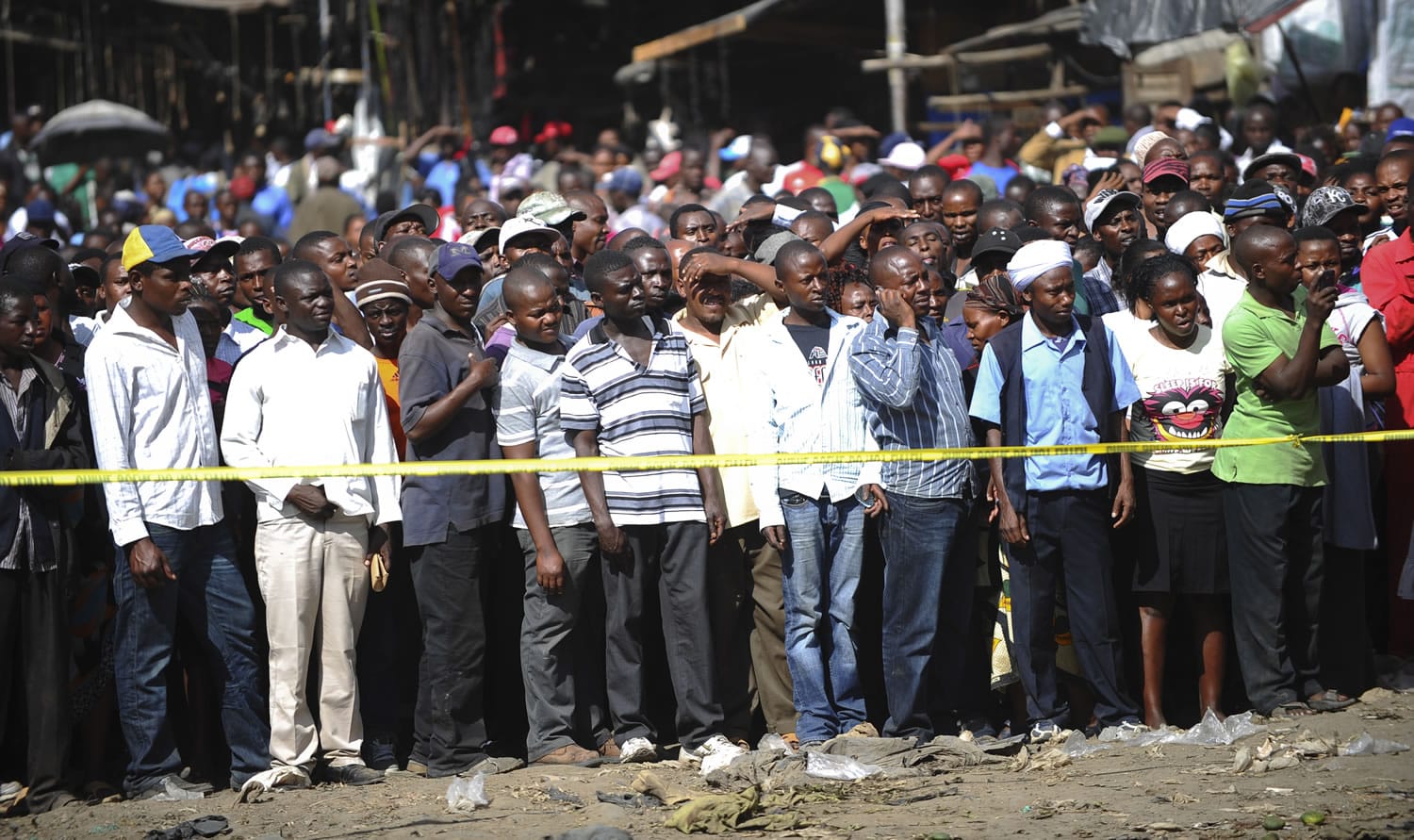 Onlookers gather behind police tape at the site where two blasts detonated, one in a mini-van used for public transportation, in a market area of Nairobi, Kenya, on Friday.
