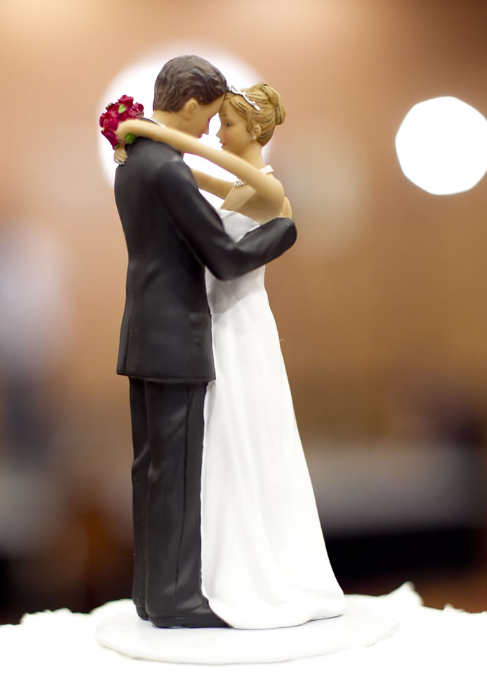 Bride and groom figurines stand atop a wedding cake.