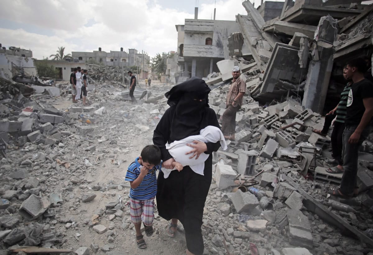 A Palestinian woman passes by rescuers inspecting the rubble of destroyed houses Aug. 4 following Israeli strikes in Rafah refugee camp, southern Gaza Strip. Amid fear that Hamas had captured an Israeli soldier, the Israeli military sealed off the Rafah area and began shelling on Aug. 1. By the end of the next day, 190 Palestinians were dead, according to a list of names compiled by two Gaza human rights groups. The suspected capture of the soldier turned out to be a false alarm and the Rafah operation is almost certain to be a focus of U.N.