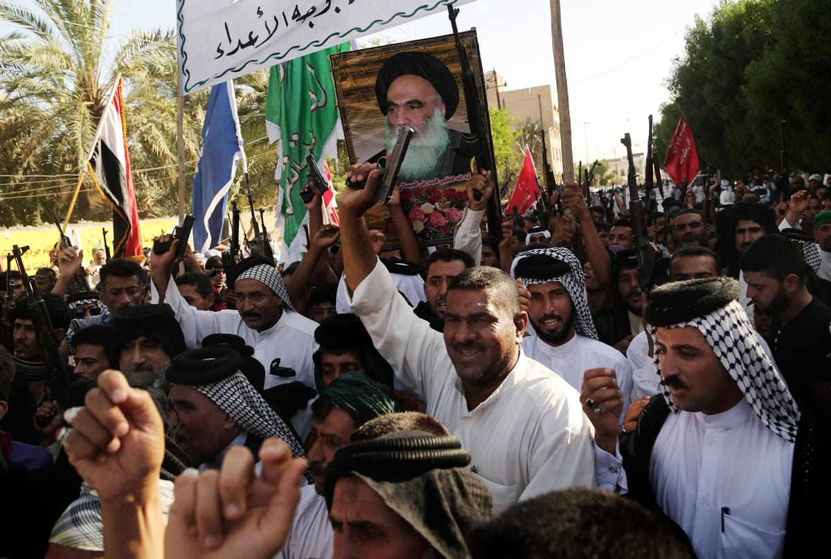 Shiite tribal fighters carry a poster of Shiite spiritual leader Grand Ayatollah Ali al-Sistani, as they raise their weapons chanting slogans against the al-Qaida-inspired Islamic State of Iraq and the Levant in Basra, Iraq's second-largest city, 340 miles southeast of Baghdad, Iraq, on Monday.