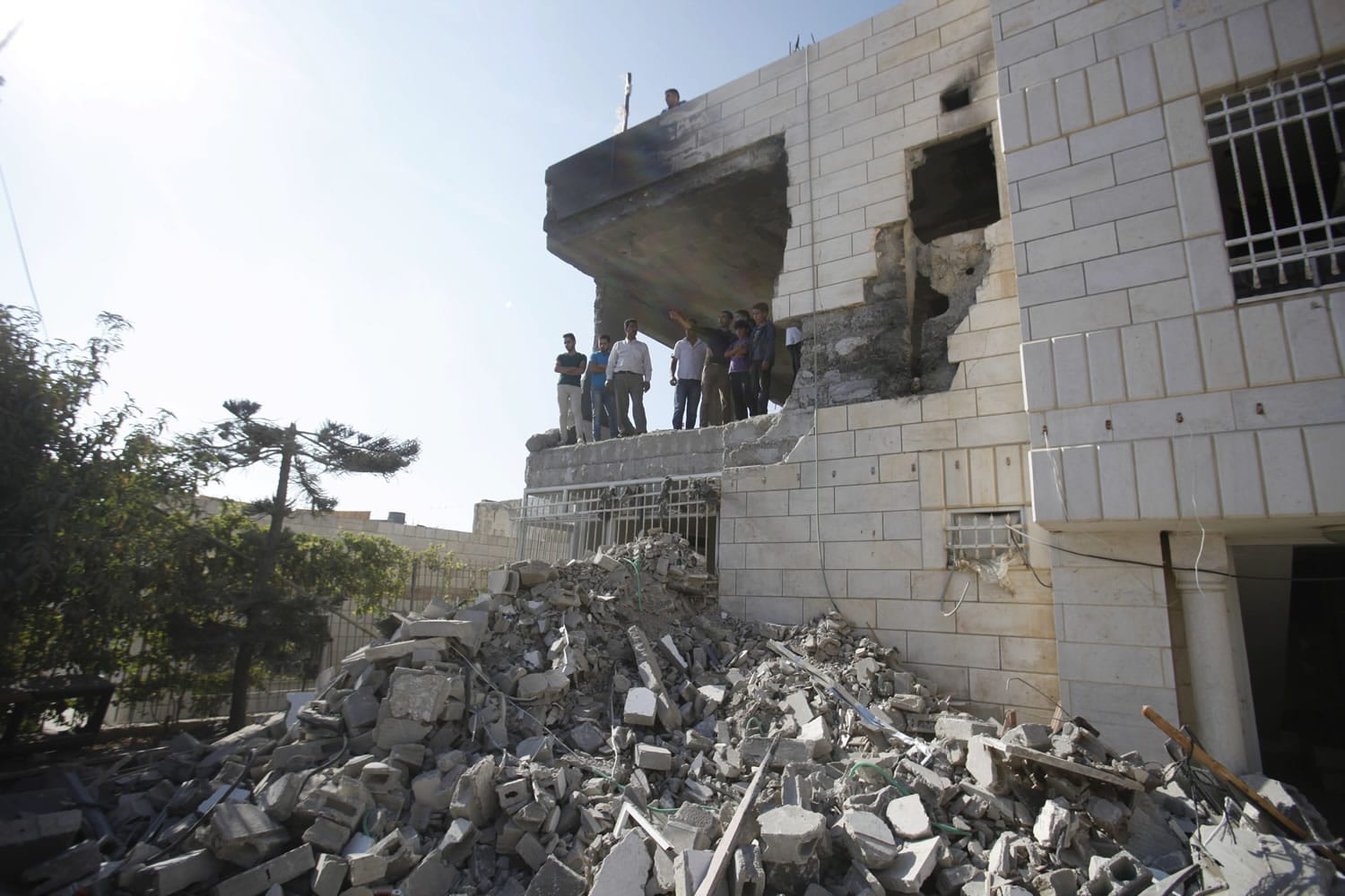 Palestinians stand in what is left of the home of Amer Abu Aisheh, one of three Palestinians identified by Israel as suspects in the killing of three Israeli teenagers, after it was demolished by the Israeli army in the West Bank city of Hebron, Monday, Aug. 18 , 2014.