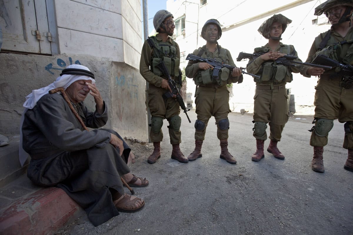 Israeli soldiers stand next to a Palestinian man Wednesday in the village of Taffouh near the West Bank city of Hebron.