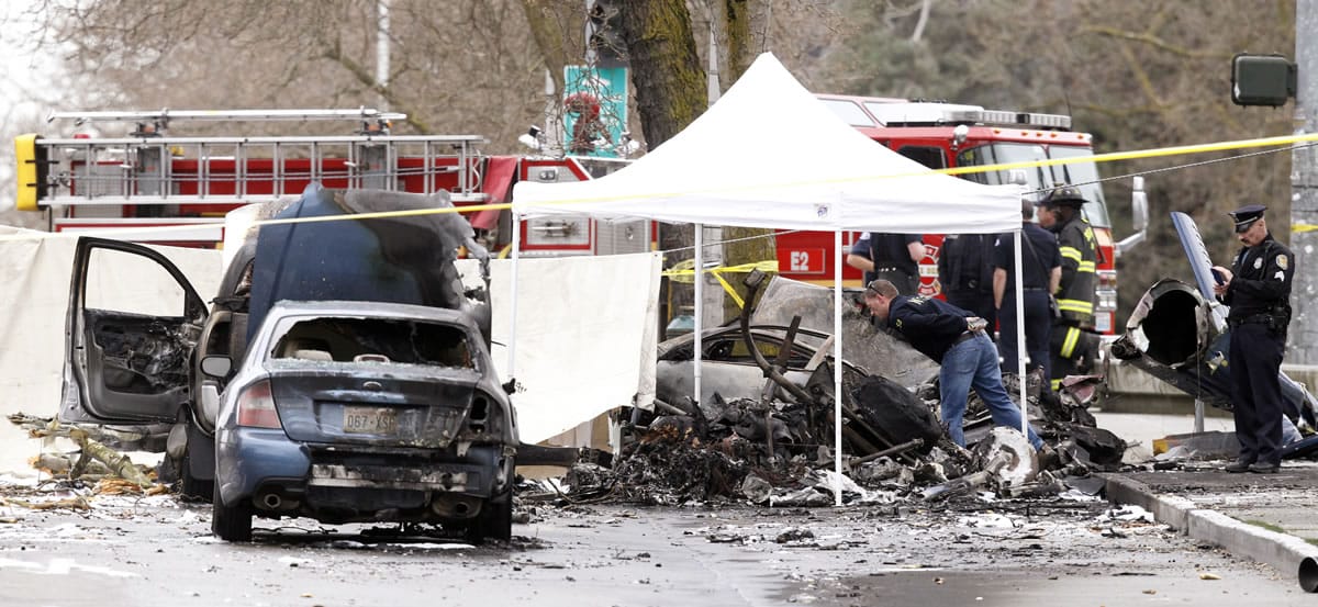 An investigator looks over the charred wreckage of a news helicopter and two vehicles after the chopper crashed into a city street near the Space Needle on Tuesday in Seattle.
