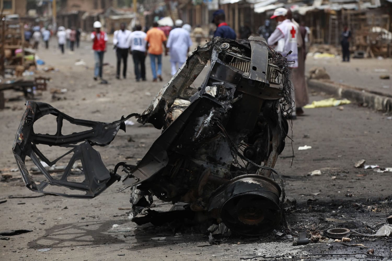 People walk past the remains of one of Tuesday's car bombs in Jos, Nigeria, on Wednesday.