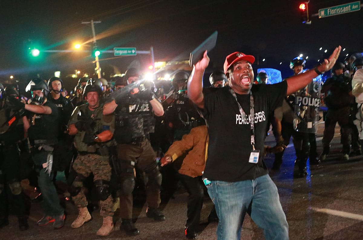 A citizen peacekeeper tries to keep protesters back as police advance Monday in Ferguson, Mo.